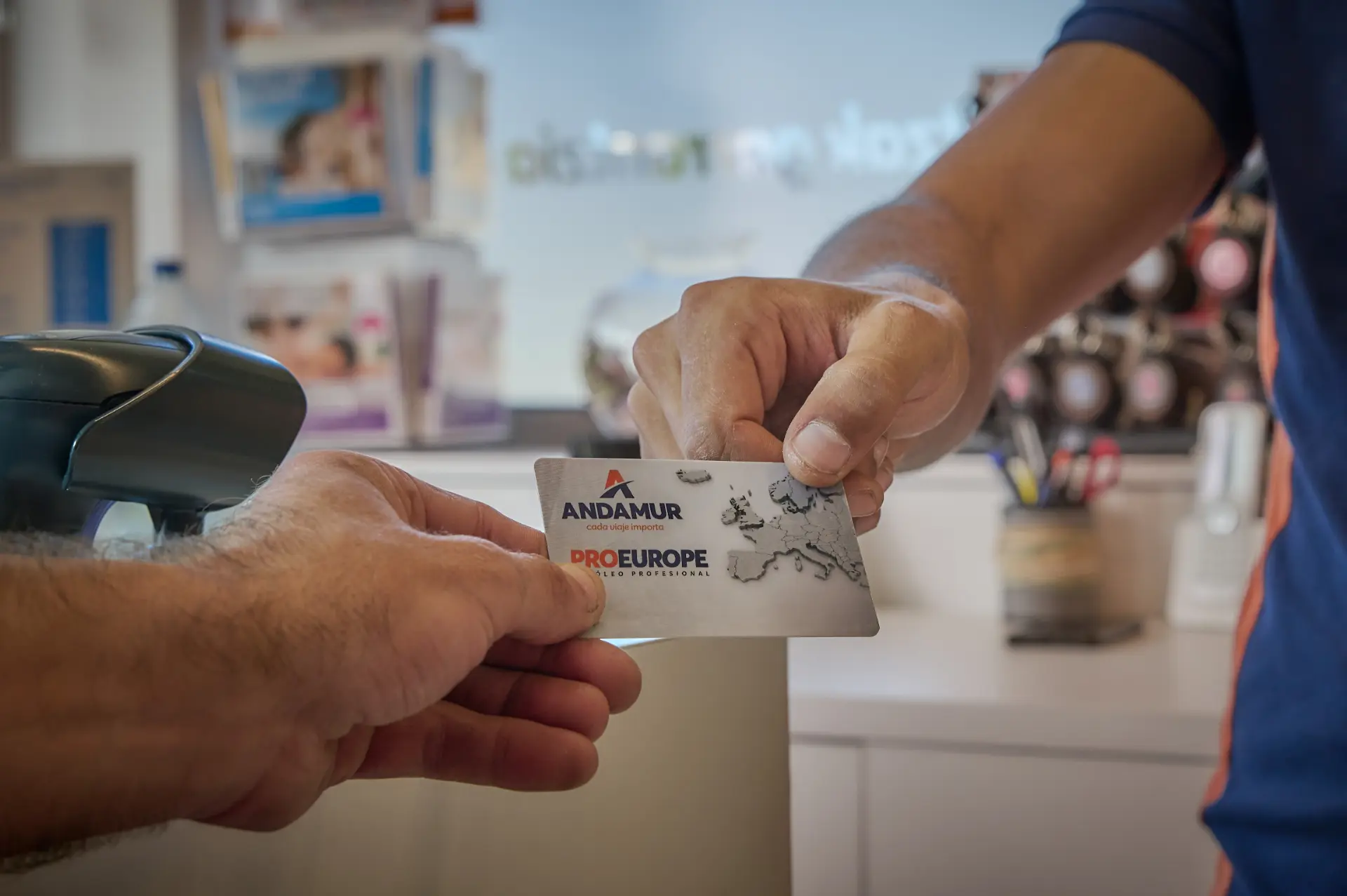 Dos personas intercambian una tarjeta Andamur ProEurope en un mostrador de una oficina o tienda, destacando cómo Andamur apoya a los conductores en las áreas de descanso de toda Europa.