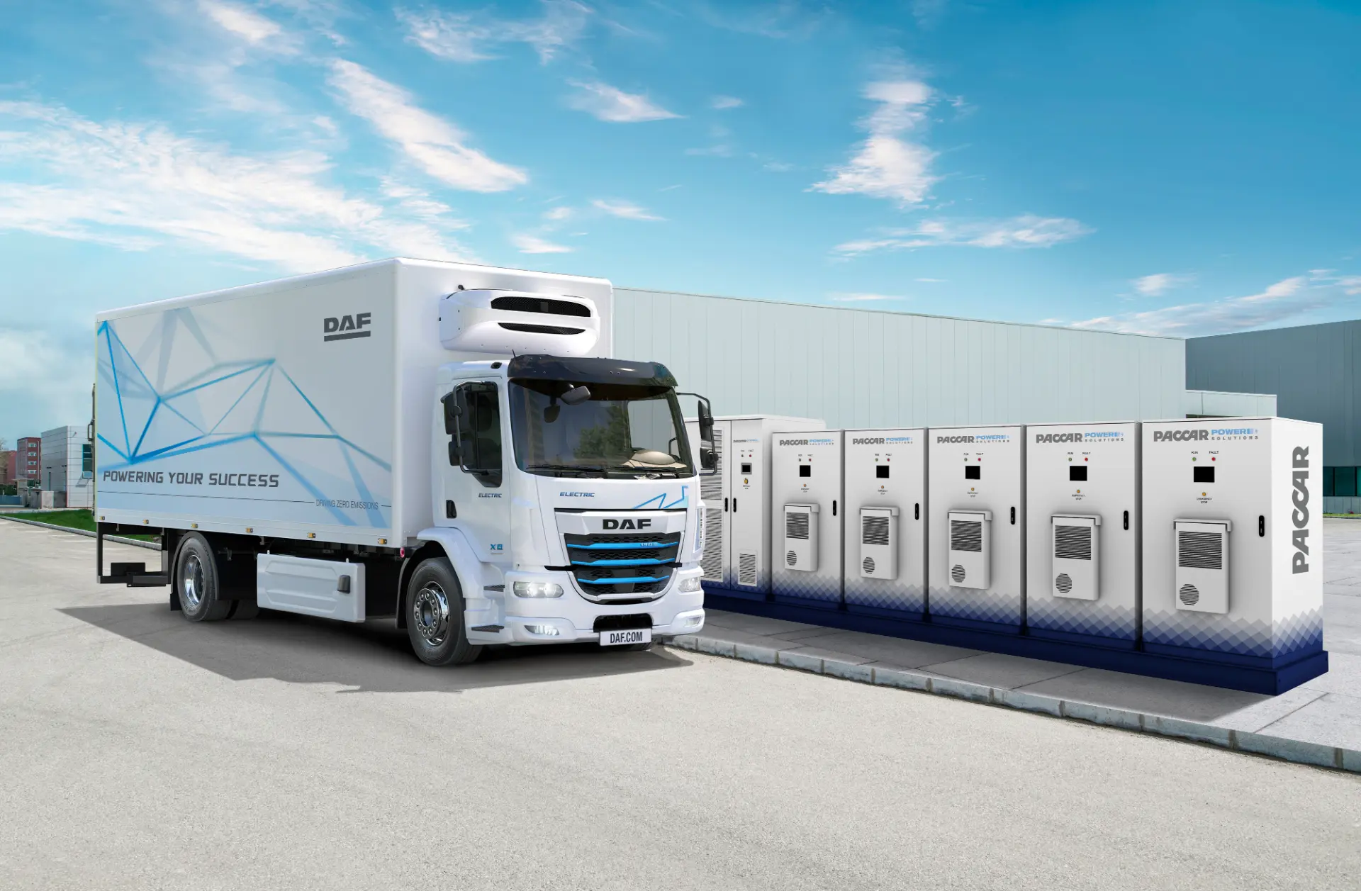 Un vehículo blanco de DAF Trucks aparcado junto a estaciones de carga eléctrica PACCAR Cero Emisiones en el exterior de una nave industrial en España.