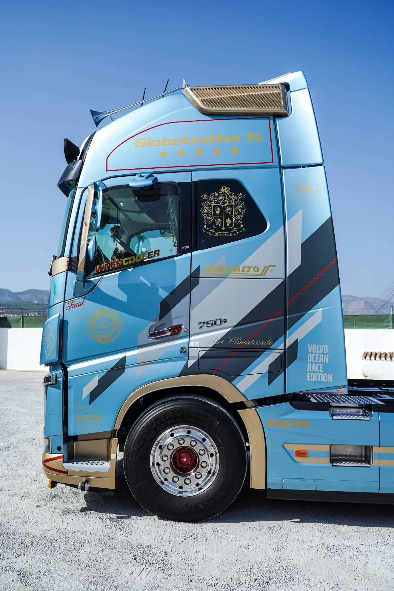 Cabina de camión Volvo Globetrotter XL azul y dorada, con borrador automático, aparcada al aire libre con montañas al fondo.