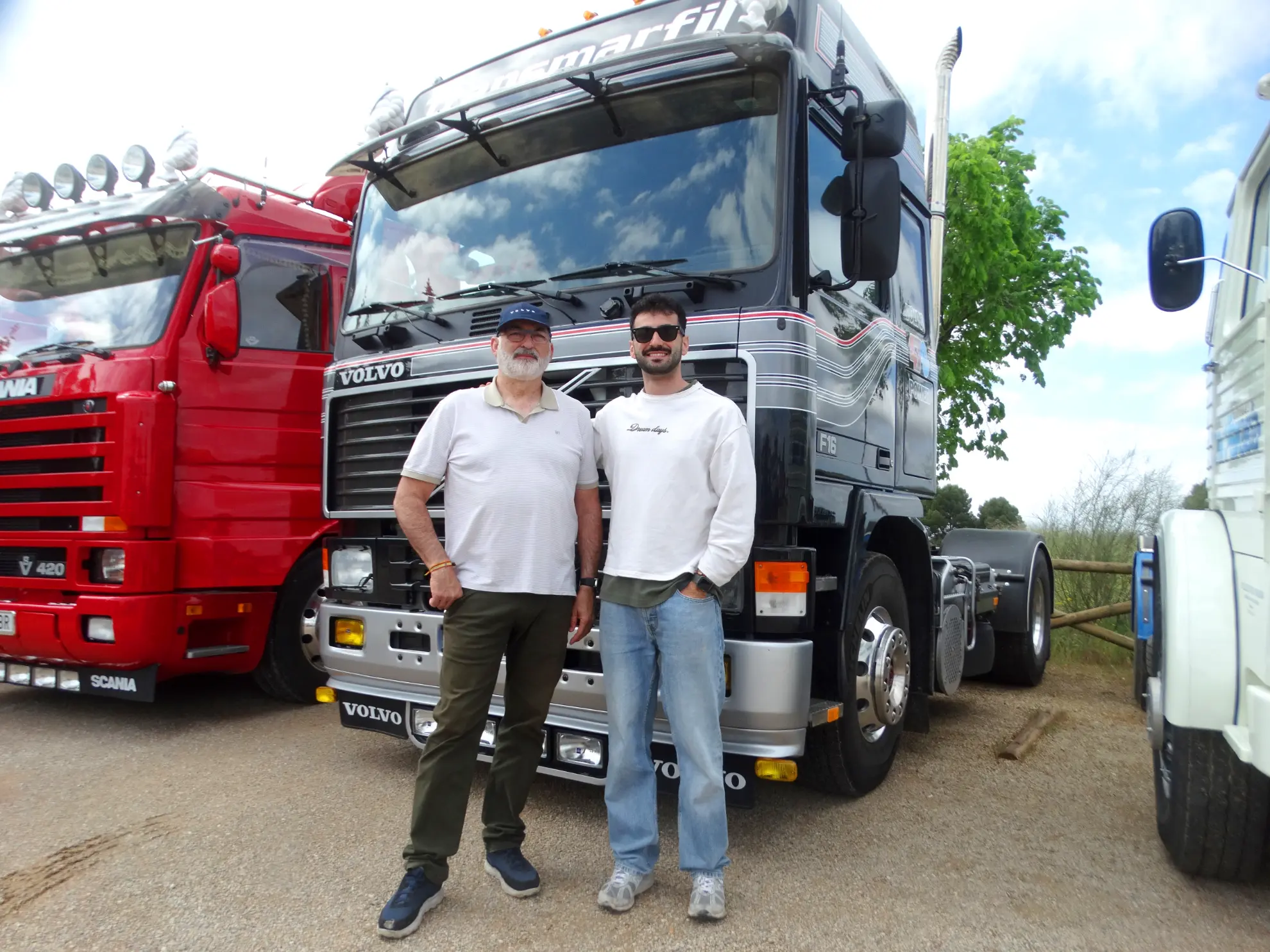 Dos hombres delante de un camión Volvo negro, con un camión rojo y otro blanco a su lado, muestran el último sistema de borrador automático para agilizar la logística.