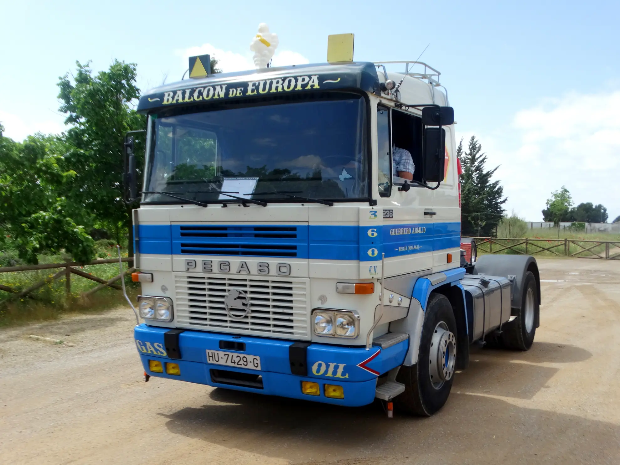 Camión Pegaso azul y blanco con un letrero "BALCON DE EUROPA" encima del parabrisas, aparcado en un camino de tierra, lleva un borrador automático montado cerca del salpicadero.
