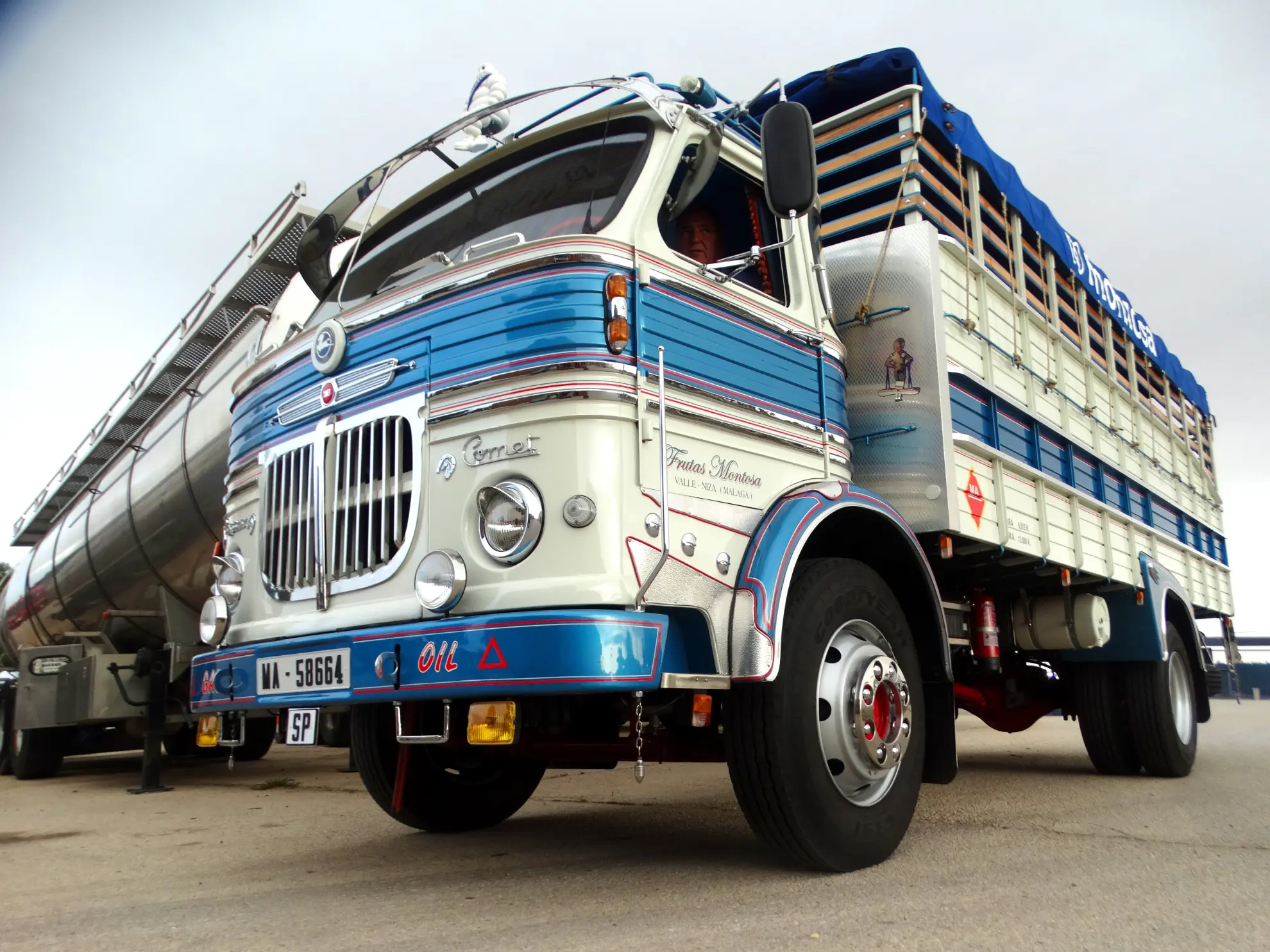 Camión clásico azul y blanco de época con detalles decorativos, un verdadero ejemplo de camiones clásicos, aparcado en una superficie pavimentada bajo un cielo nublado.