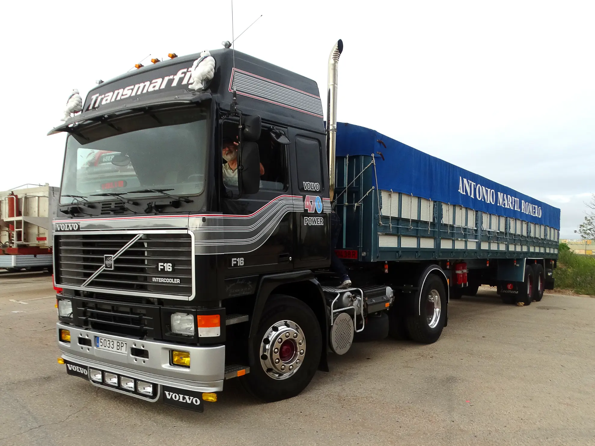 Semirremolque Volvo F16 negro con remolque cubierto azul, aparcado en un solar asfaltado, vista lateral. Destacado entre los camiones clásicos, está listo para la Vuelta a La Mancha 2025.