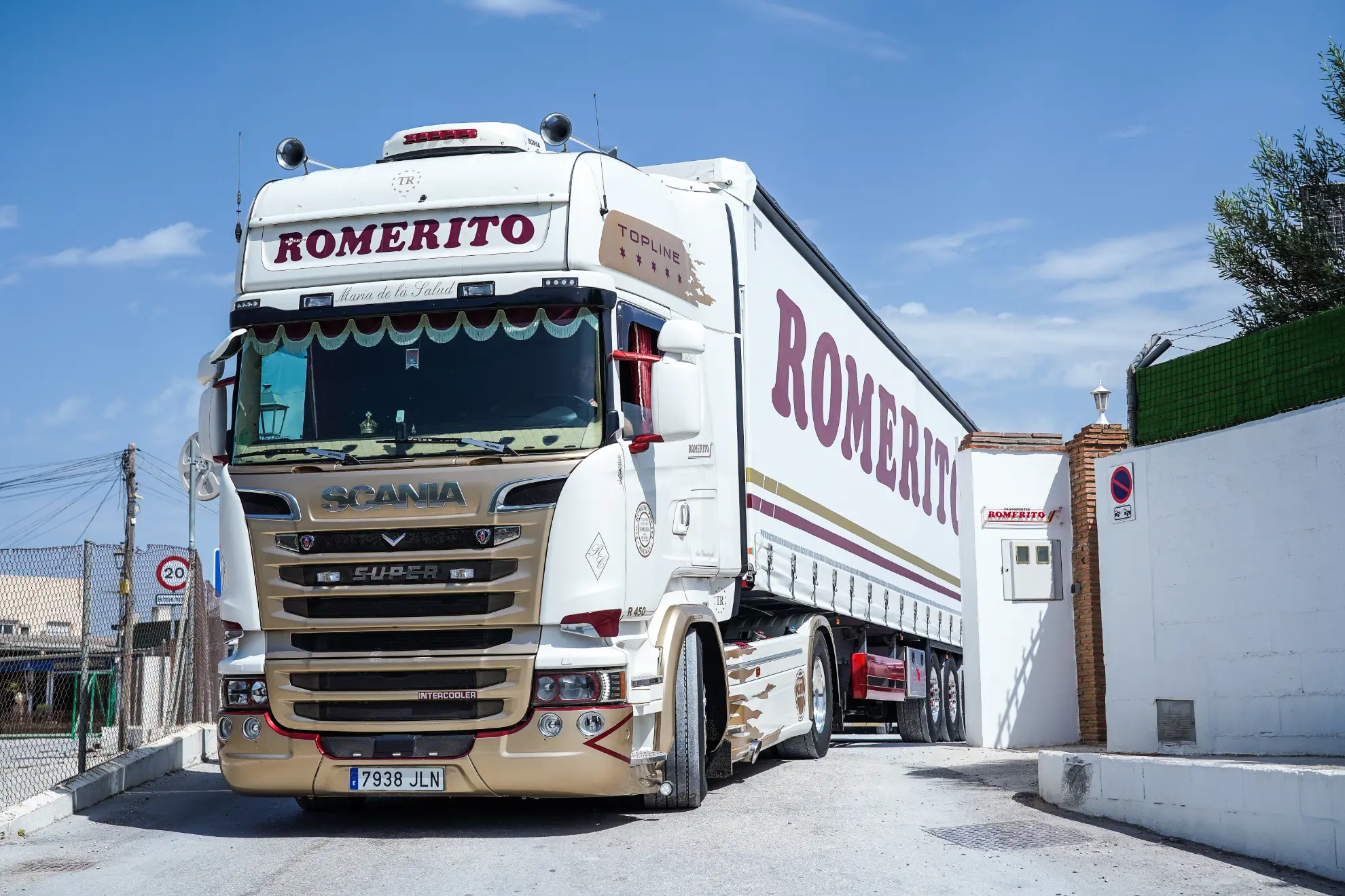 Un camión Scania blanco de la marca Romerito con Borrador automático entra en una zona industrial cerrada en un día soleado.