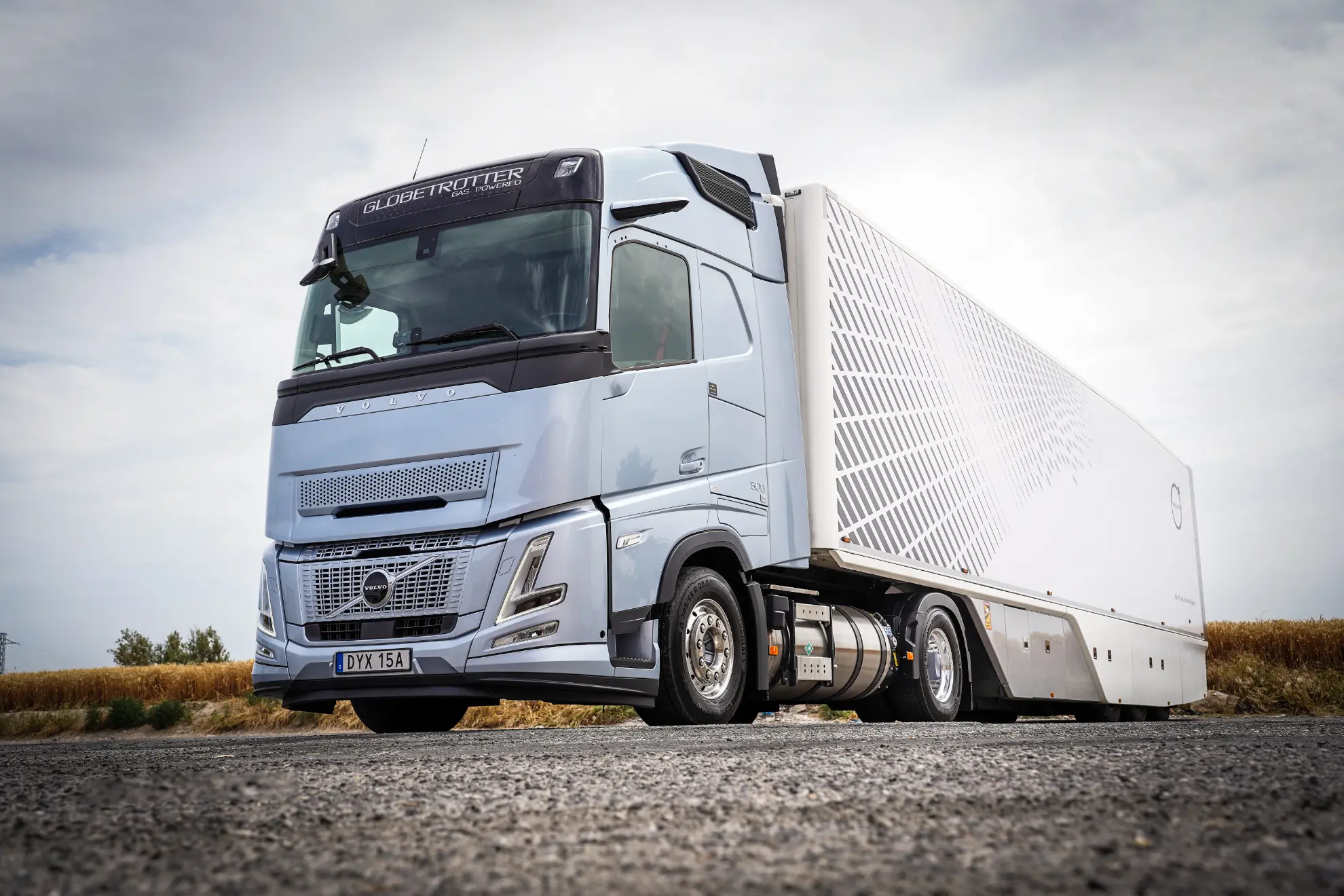 Un moderno semirremolque Volvo GNL plateado con un remolque geométrico, parte de la nueva ola de camiones a gas, está aparcado en un camino rural.