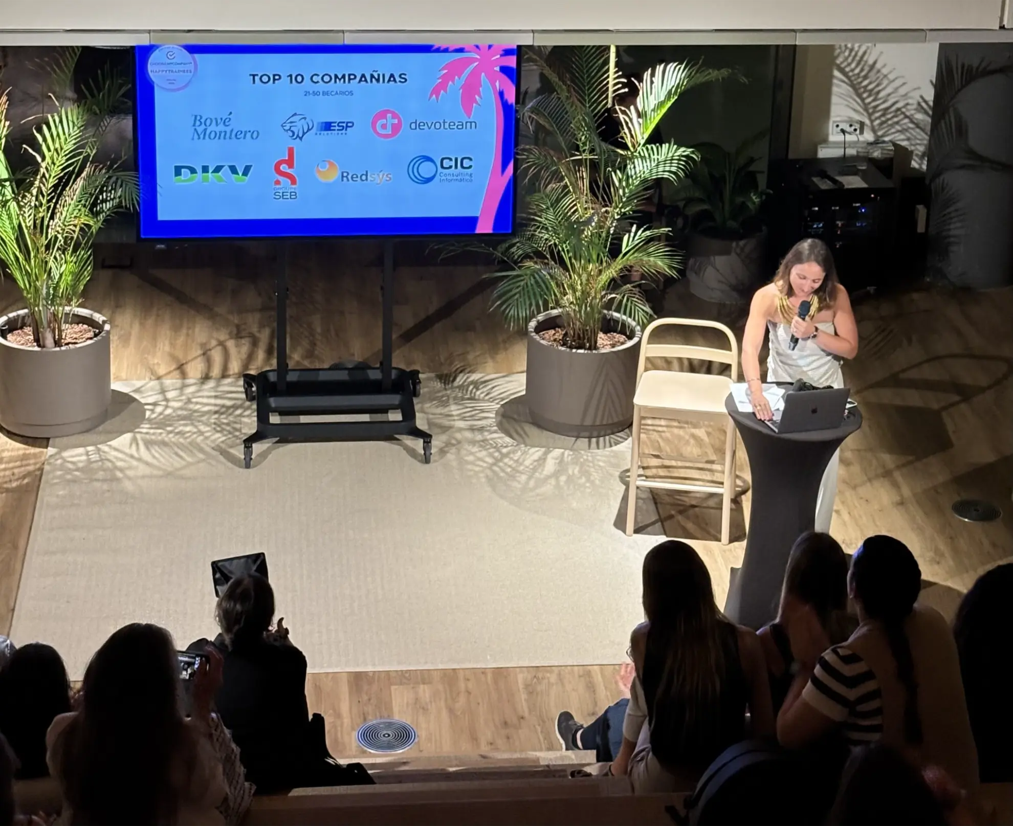 Una mujer habla en un podio frente a un público mientras una pantalla muestra las 10 mejores empresas para trabajar, entre ellas ESP Solutions.