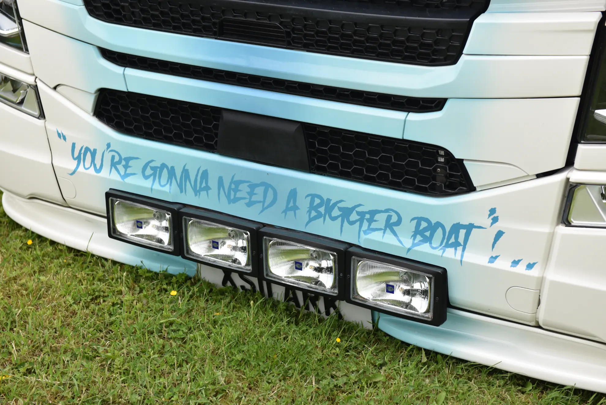 Frontal de un camión blanco customizado, posiblemente un Scania 770 S, con la frase "You're gonna need a bigger boat" pintada en azul, un claro guiño a Tiburón.