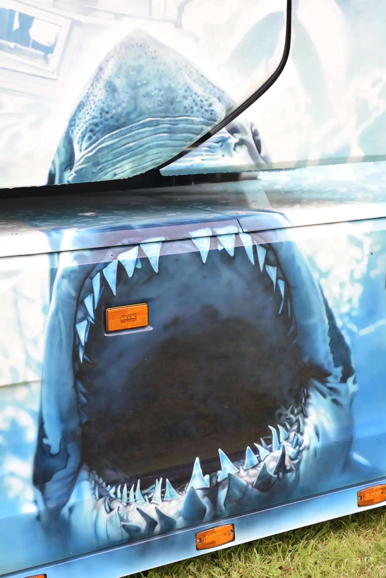 Una feroz boca de tiburón con las fauces abiertas está pintada en el lateral de un Scania 770 S, sus afilados dientes contrastan sobre un fondo azul agua, haciendo que este camión customizado realmente destaque.