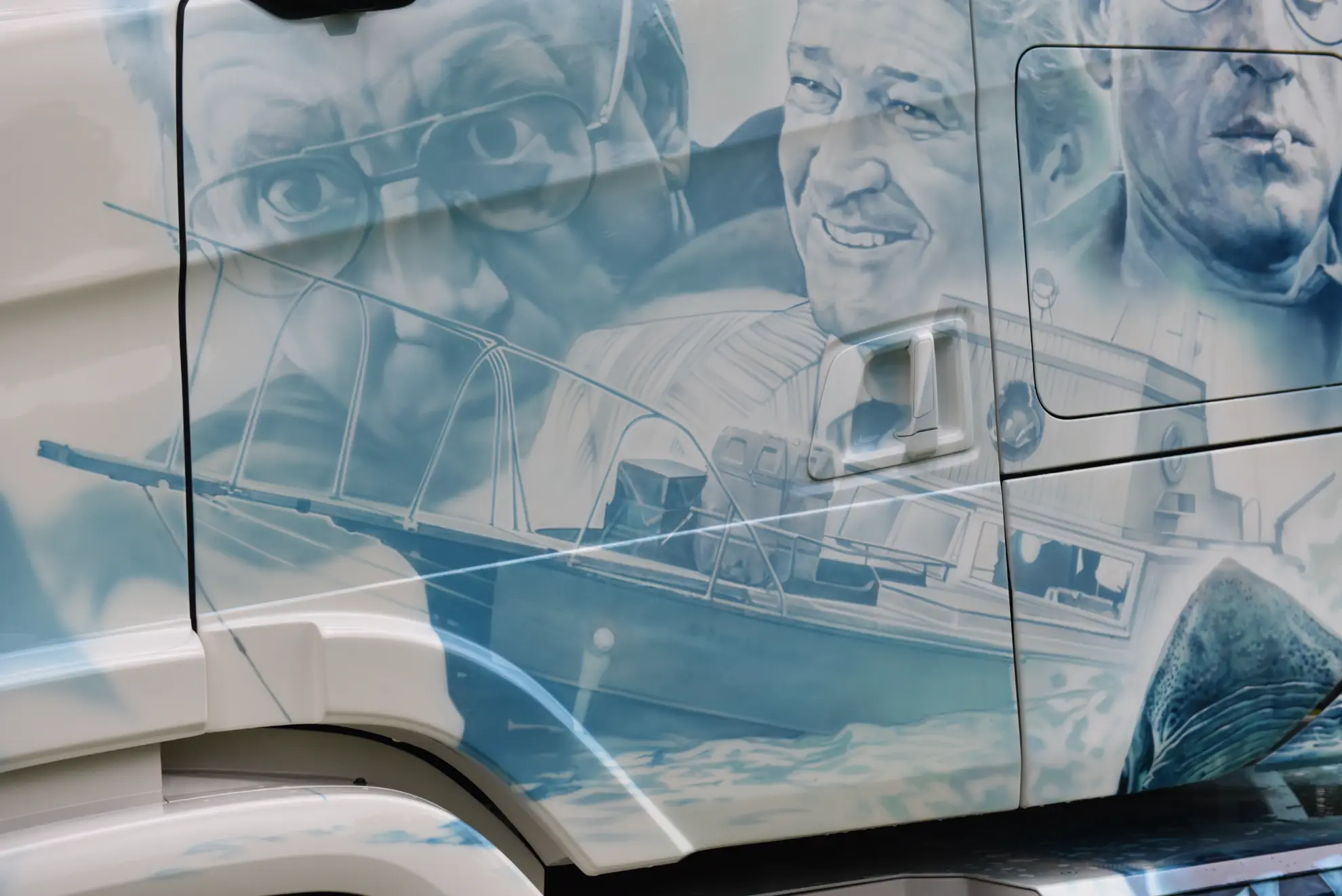 El arte aerografiado de un camión personalizado muestra las caras de tres hombres y un barco, que se exhiben en la puerta del conductor.