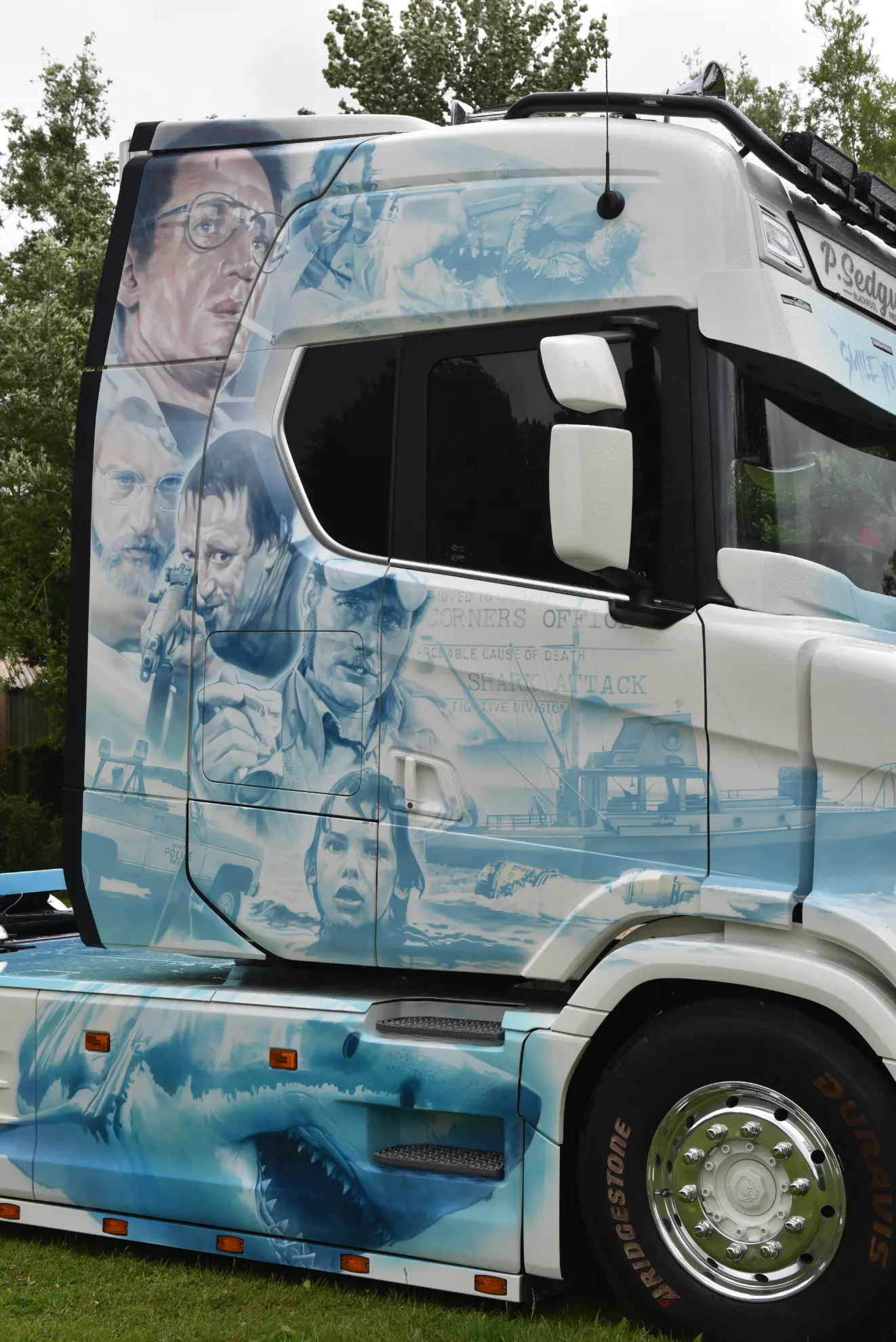 Un Scania 770 S camión blanco personalizado luce en su lateral un detallado arte con aerógrafo de escenas y personajes de la película "Tiburón".