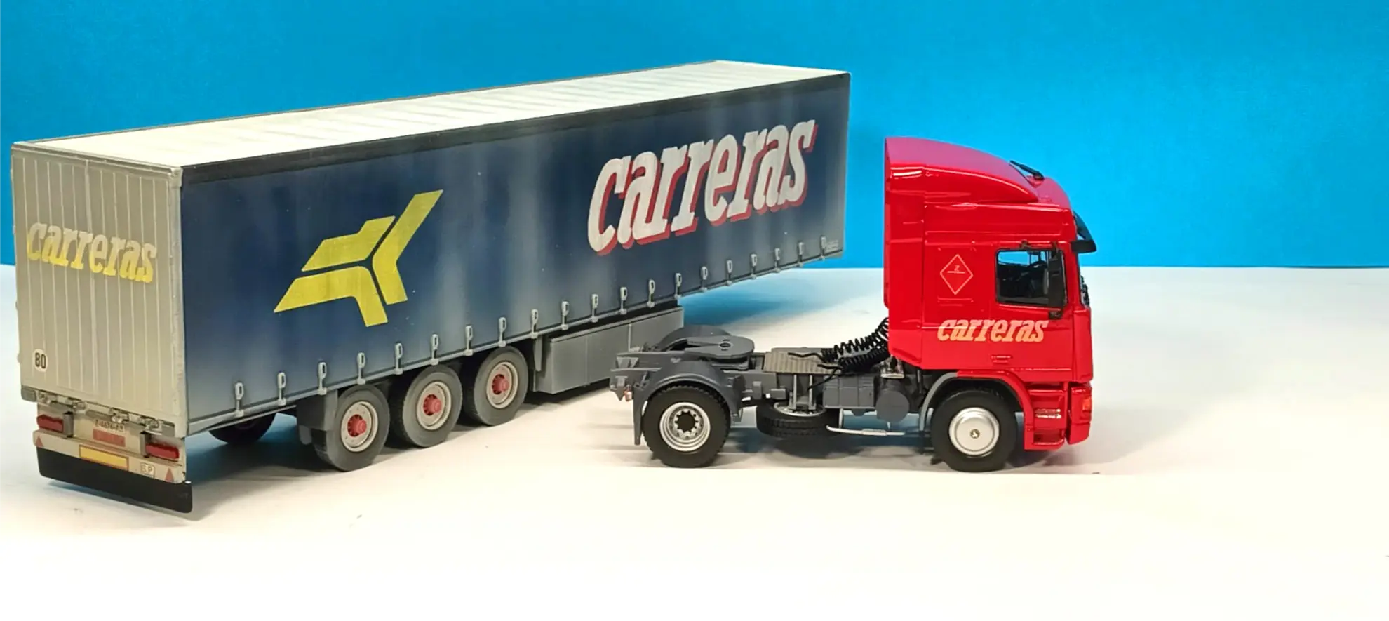 Camión y remolque Carrera rojos con marca, estacionados sobre una superficie blanca sobre fondo azul: una impresionante réplica camión personalizada perfecta para los fans de los camiones Italeri y los coleccionistas de camiones a escala 1:24.