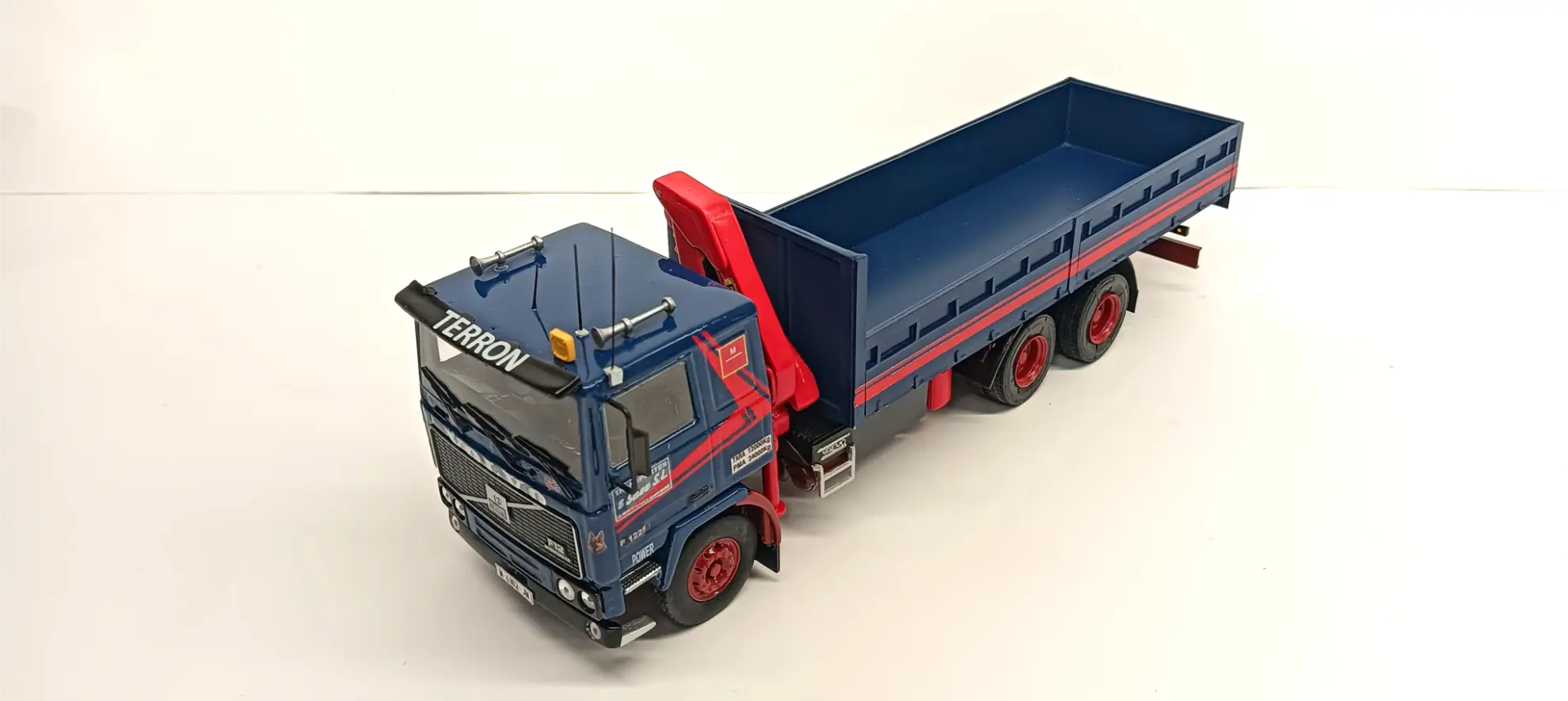 Un modelo de camión volquete azul y rojo con "TERRON" en el parabrisas, visto desde arriba sobre un fondo blanco: la inspiración perfecta si estás explorando cómo hacer una maqueta de camión.