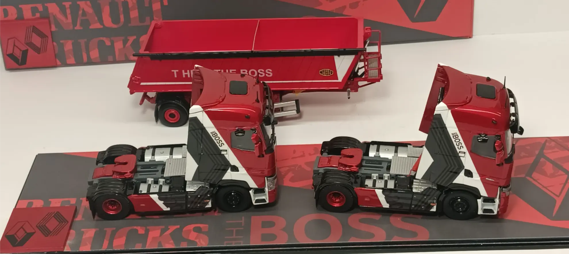 Dos camiones rojos y blancos a escala 1:24 Renault, junto a un remolque a juego, se exhiben sobre una superficie con la marca, mostrando cómo una réplica camión personalizada puede destacar en tu colección.