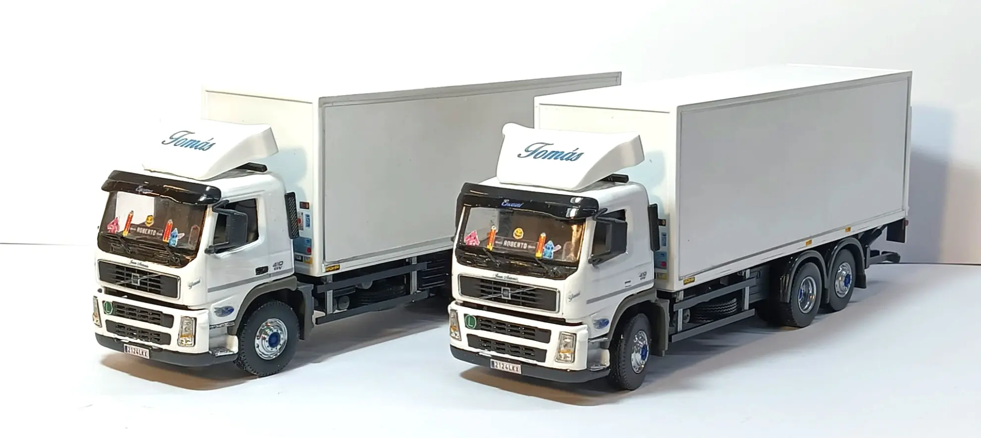 Dos camiones frigoríficos blancos con "Tomás" escrito sobre el parabrisas, aparcados uno al lado del otro, parecen la inspiración perfecta para una réplica de camión personalizada o para los que están aprendiendo cómo hacer una maqueta de camión.