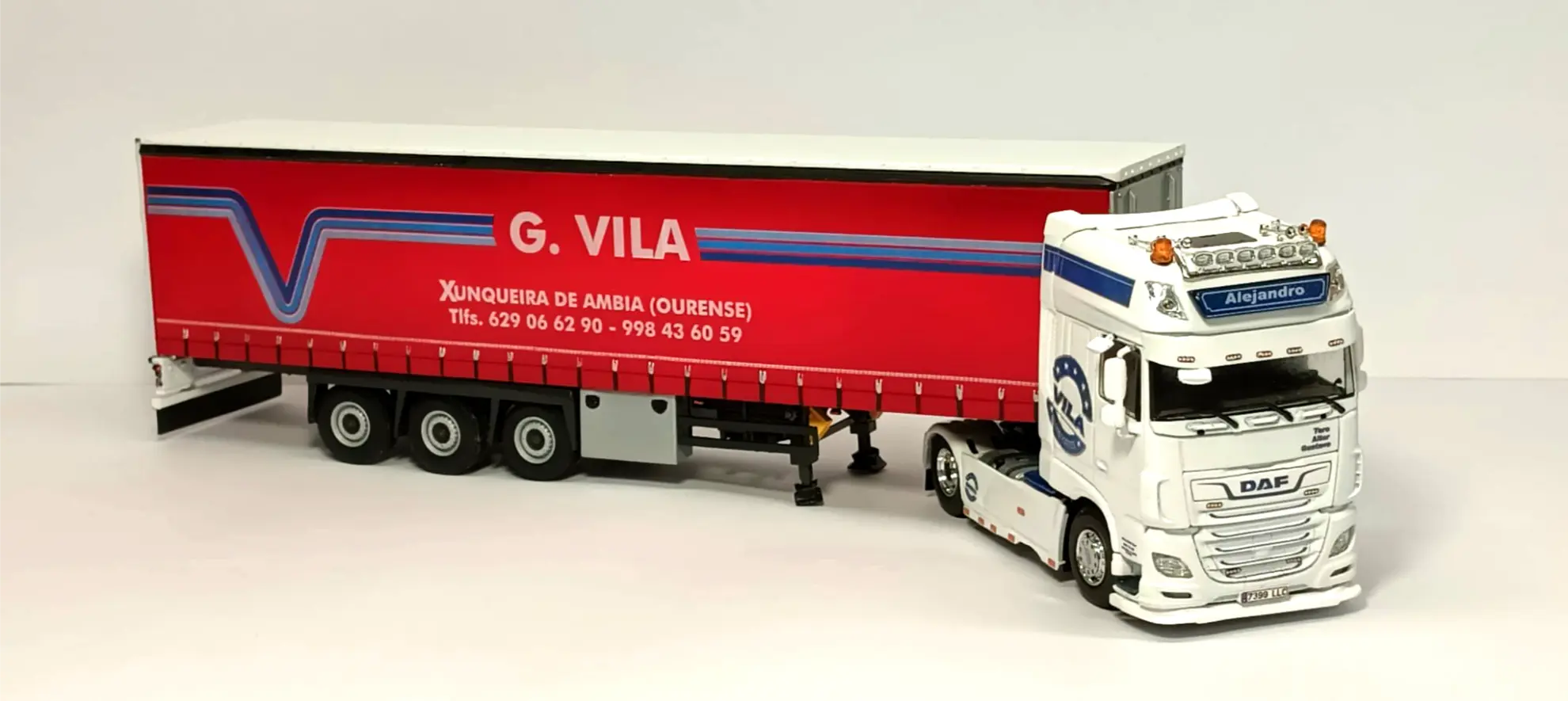 Maqueta de camión y remolque con "G. VILA" e información de contacto en el remolque rojo, aparcada sobre una superficie blanca, perfecta para los aficionados a las maquetas de camiones o los interesados en cómo hacer una maqueta de camión.