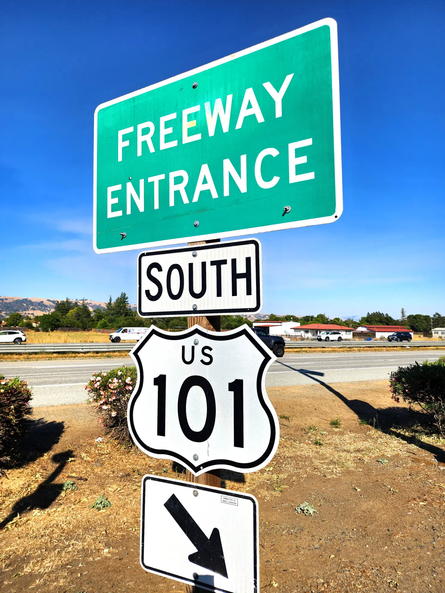 Señal verde de "Freeway Entrance" sobre "South US 101" y flechas al borde de la carretera en un día soleado, captada con la nitidez de un borrador automático.