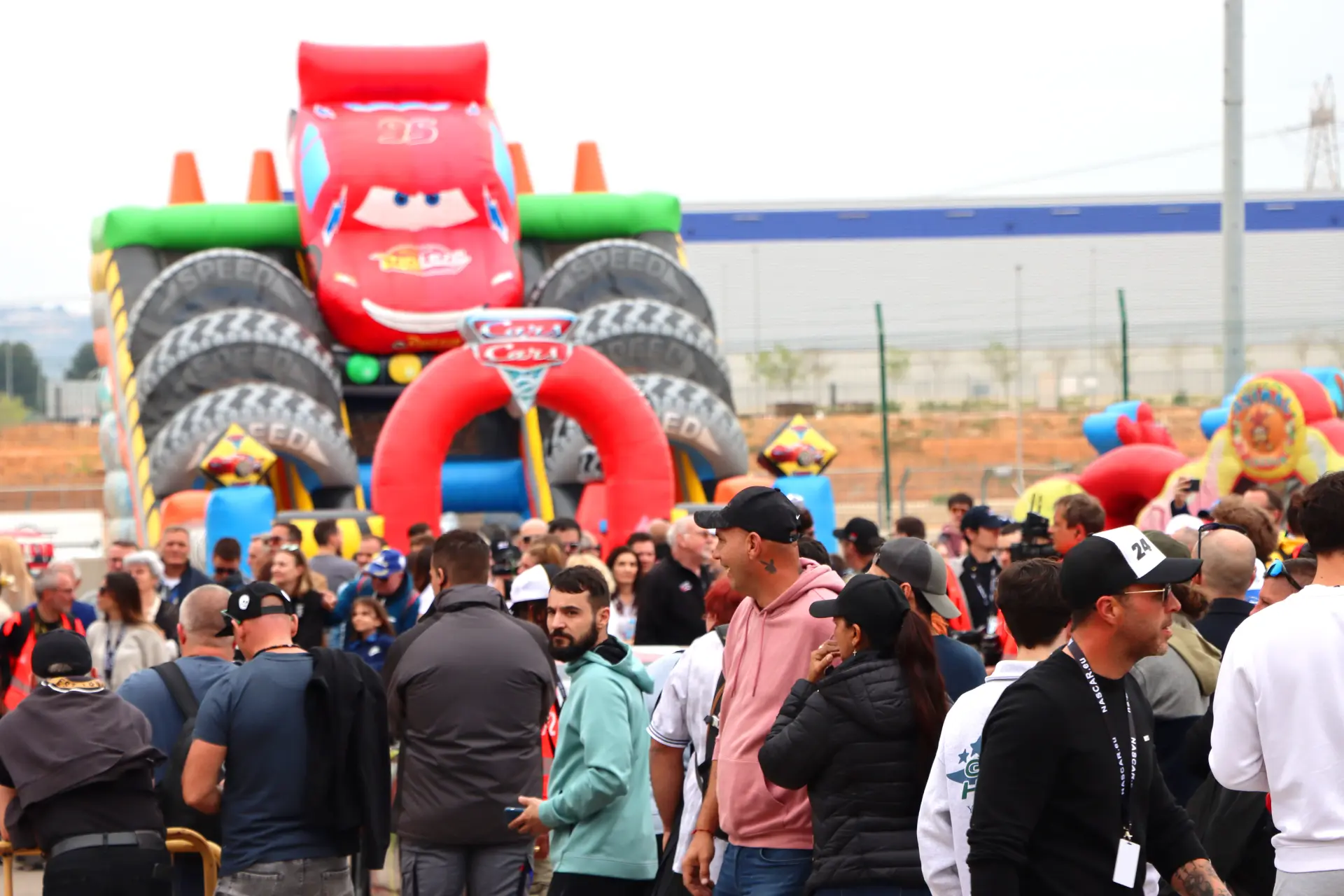 Una multitud se reúne cerca de un gran tobogán hinchable para coches, al estilo del Rayo McQueen de Cars.
