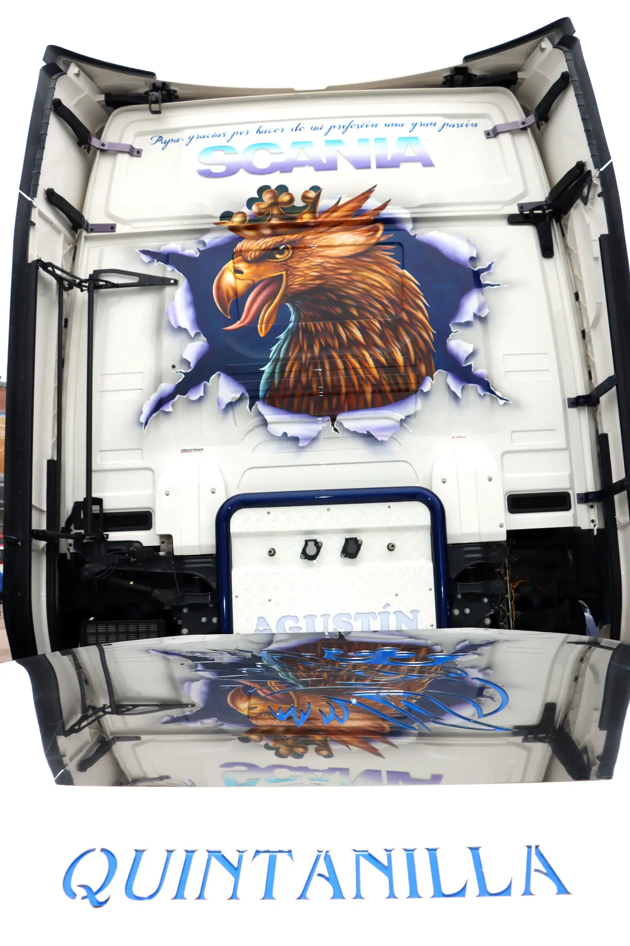 Arte trasero de camión de un águila coronada rompiendo el metal, con "Quintanilla" y una frase cursiva azul encima.