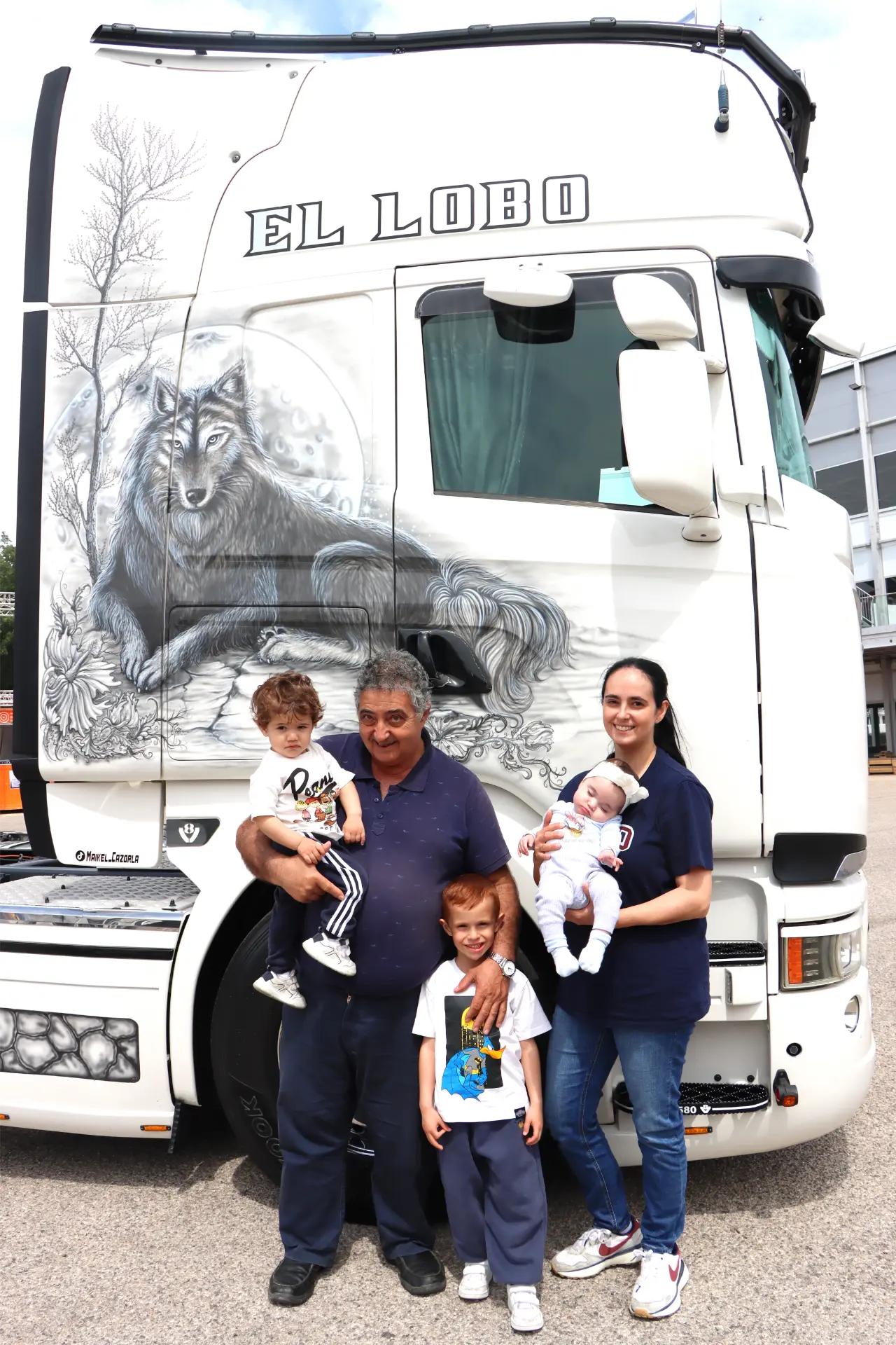 Una familia sonriente delante de un camión blanco con un detallado mural de lobos y las palabras "EL LOBO".