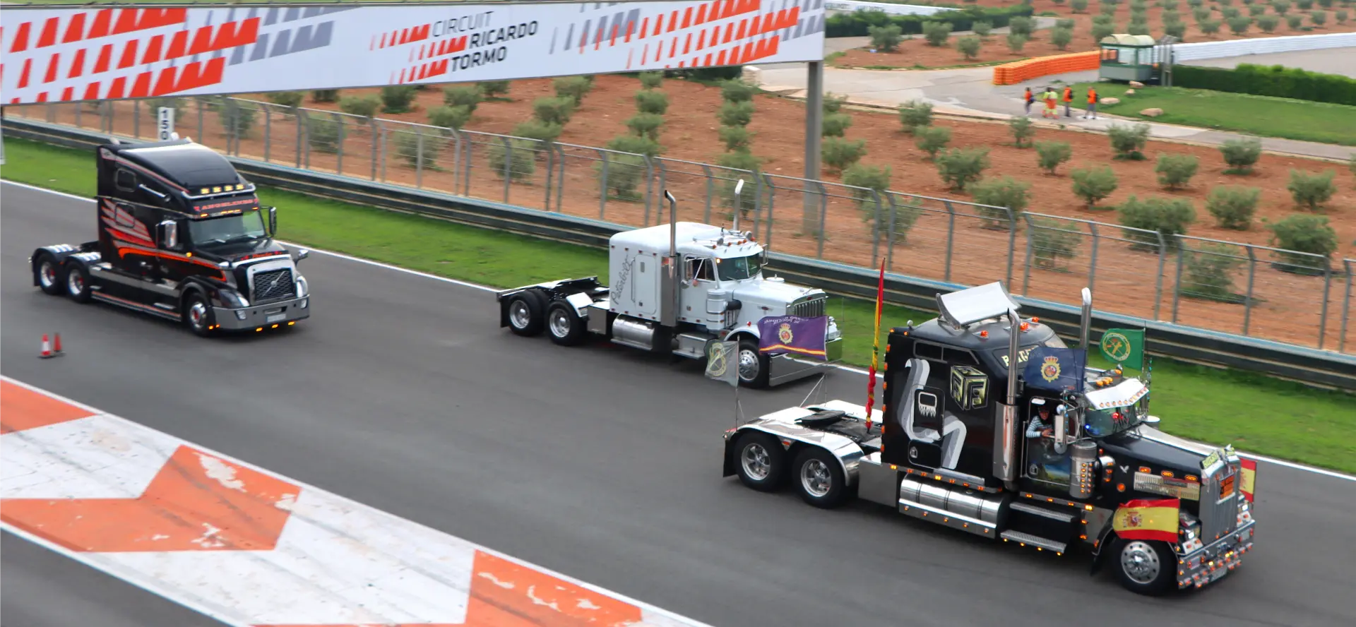 Tres semirremolques decorados circulan por un circuito del Circuit Ricardo Tormo, rodeado de campos verdes.