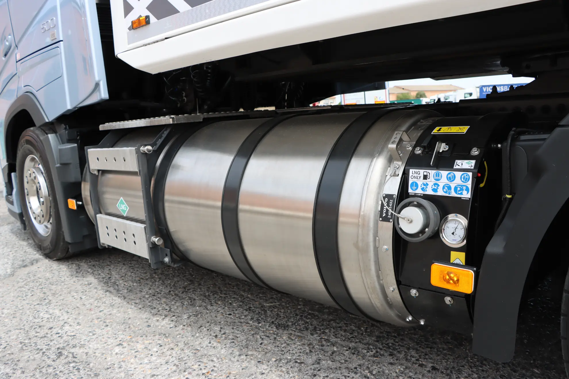 Primer plano del gran depósito cilíndrico de combustible de un camión Volvo con indicadores y etiquetas de seguridad, aparcado sobre el asfalto.