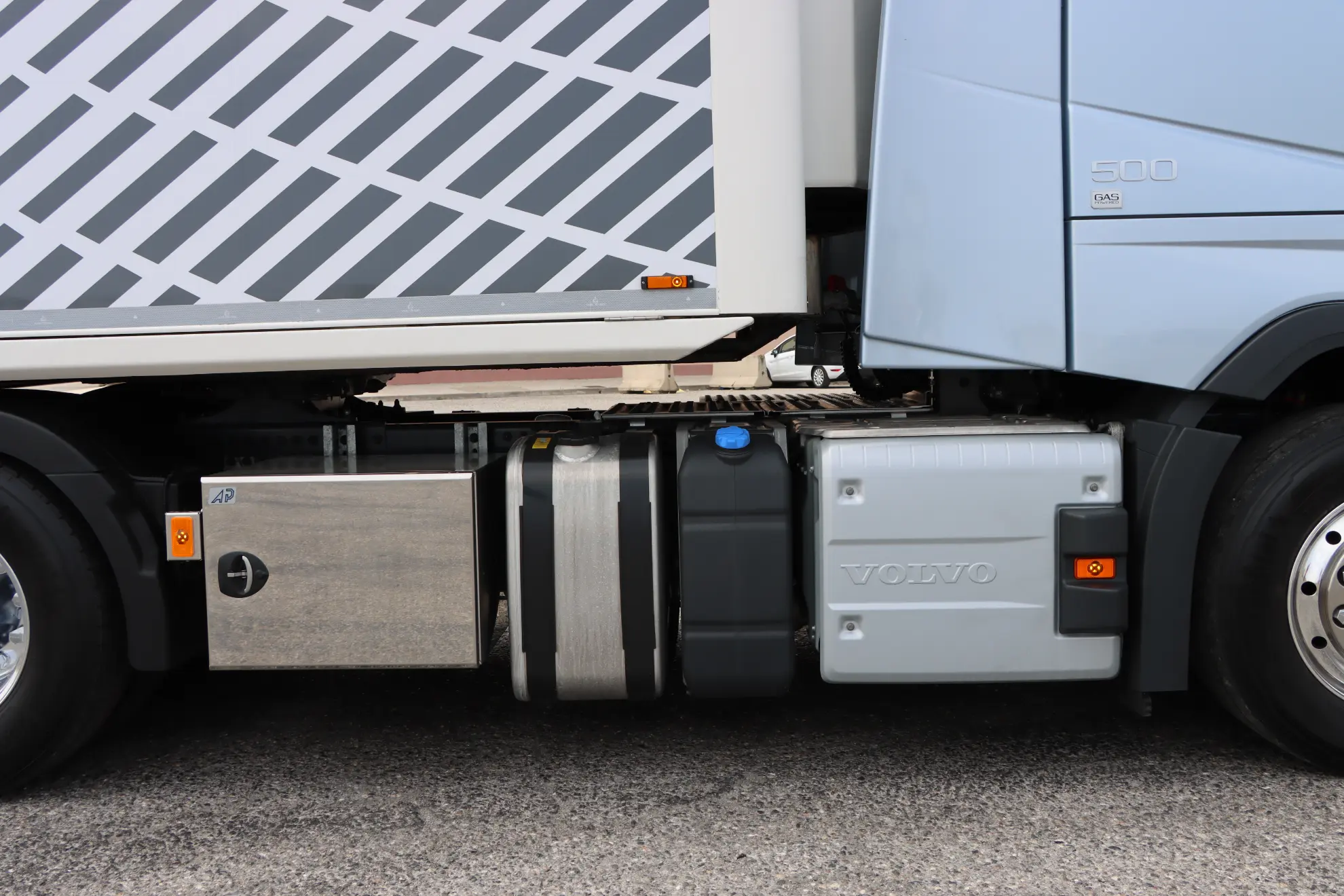 Vista lateral de un camión Volvo a gas mostrando su depósito de combustible y parte de la cabina cerca de un remolque estampado-ideal para cualquier gestor de flotas considerando eficiencia o comprobando precio GNL España.