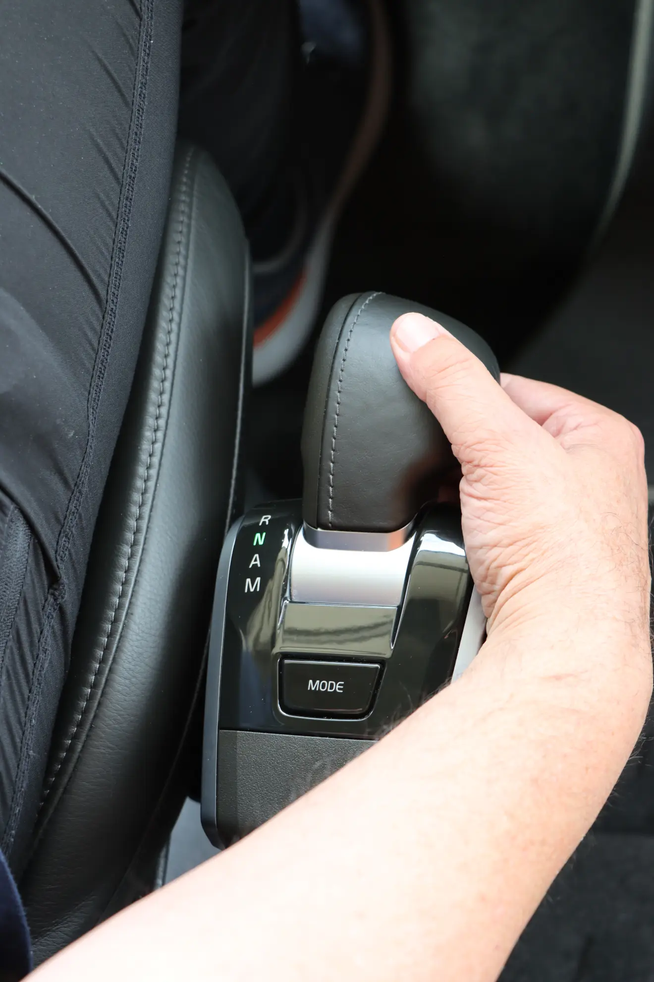 Mano sujetando la palanca de cambios de un coche con las posiciones de las marchas y un botón de "modo" visible, ideal para gestor de flotas explorando vehículos innovadores como camiones a gas o modelos volvo gnl.