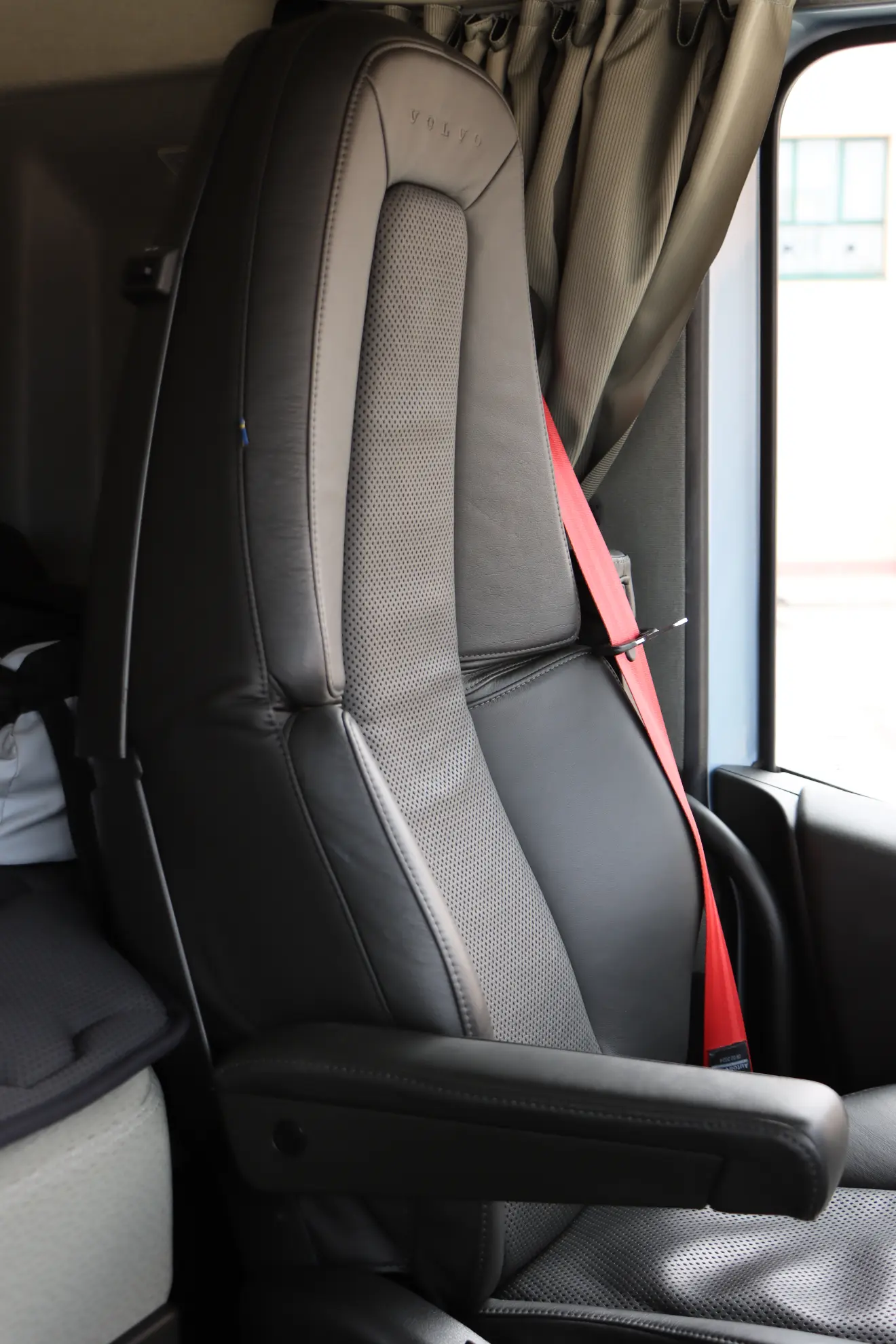 Asiento de camión de cuero negro con reposabrazos y cinturón de seguridad rojo en el interior de una cabina de un vehículo Volvo a gas.