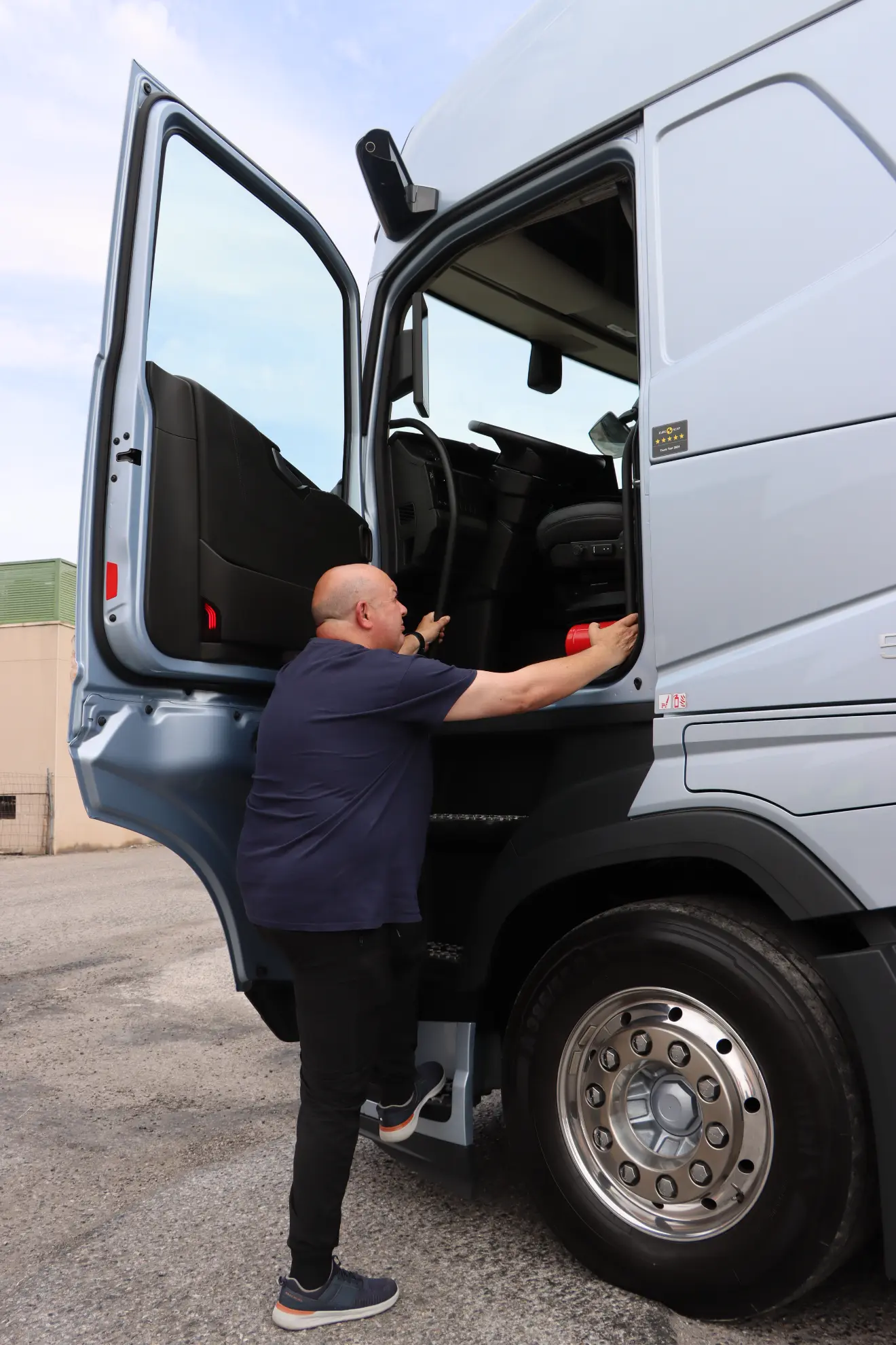 Un hombre sube a un gran camión Volvo GNL plateado con la puerta del conductor abierta.