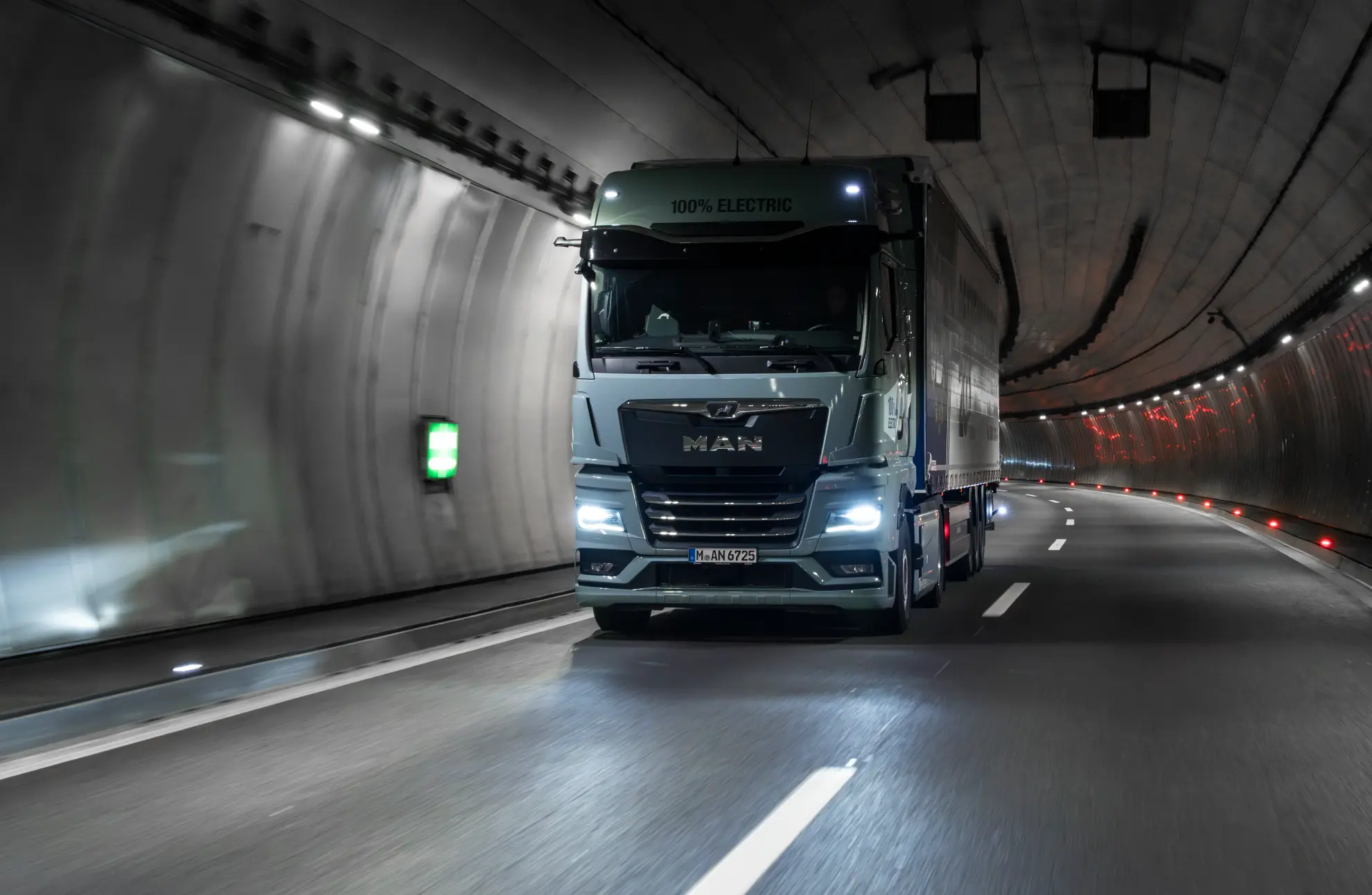 Un gran camión eléctrico atraviesa un túnel bien iluminado con superficies reflectantes y marcas viales.