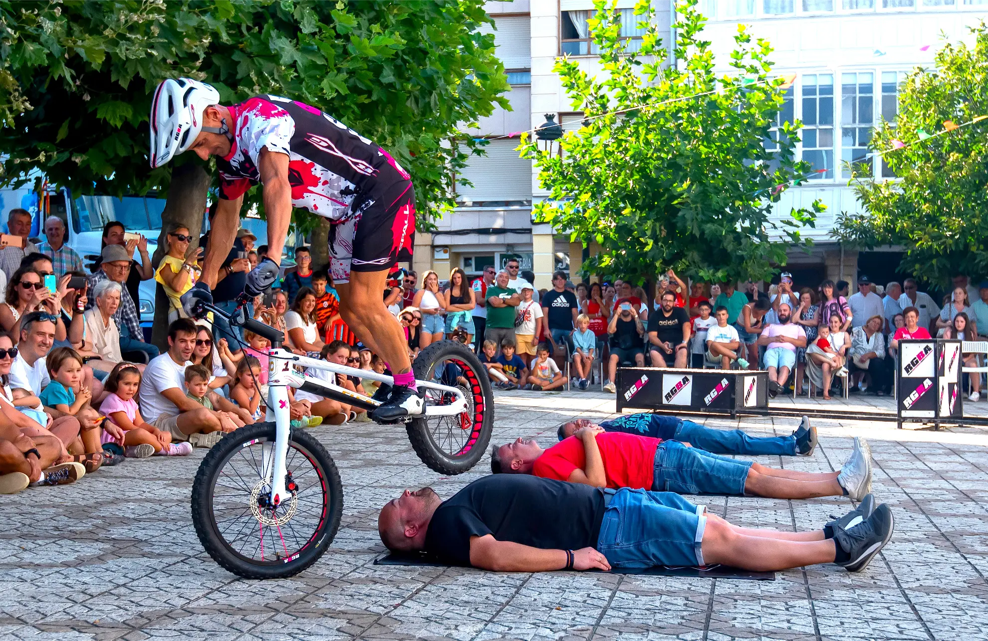 Durante la Quedada de Camiones en Soncillo 2025, un ciclista realiza una audaz acrobacia al pasar por encima de tres hombres tendidos en el suelo ante una multitud.