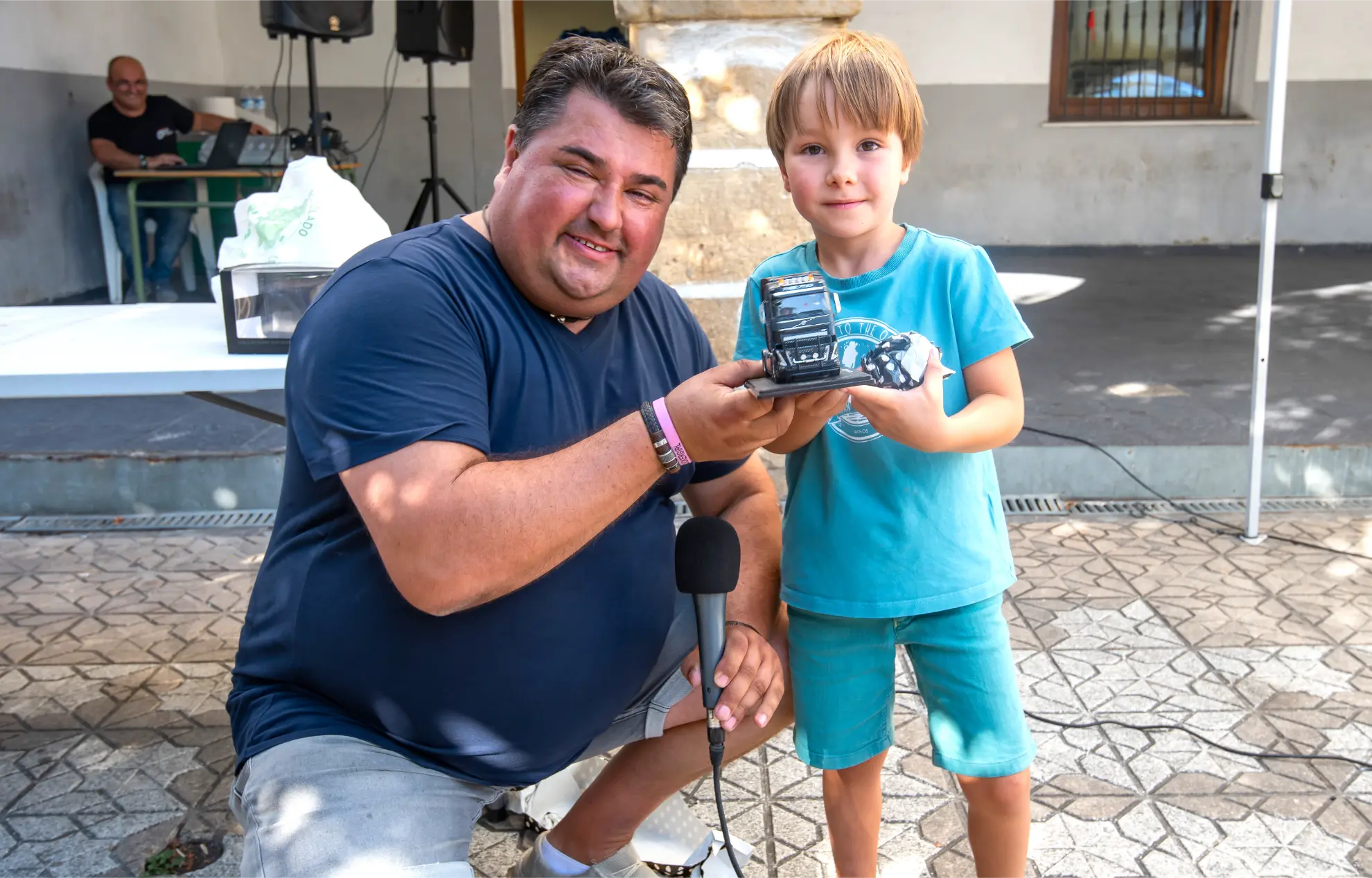 Hombre y niño sonrientes sosteniendo vehículos de juguete al aire libre, posando juntos para una foto en un día soleado en la Quedada de Camiones Soncillo 2025.