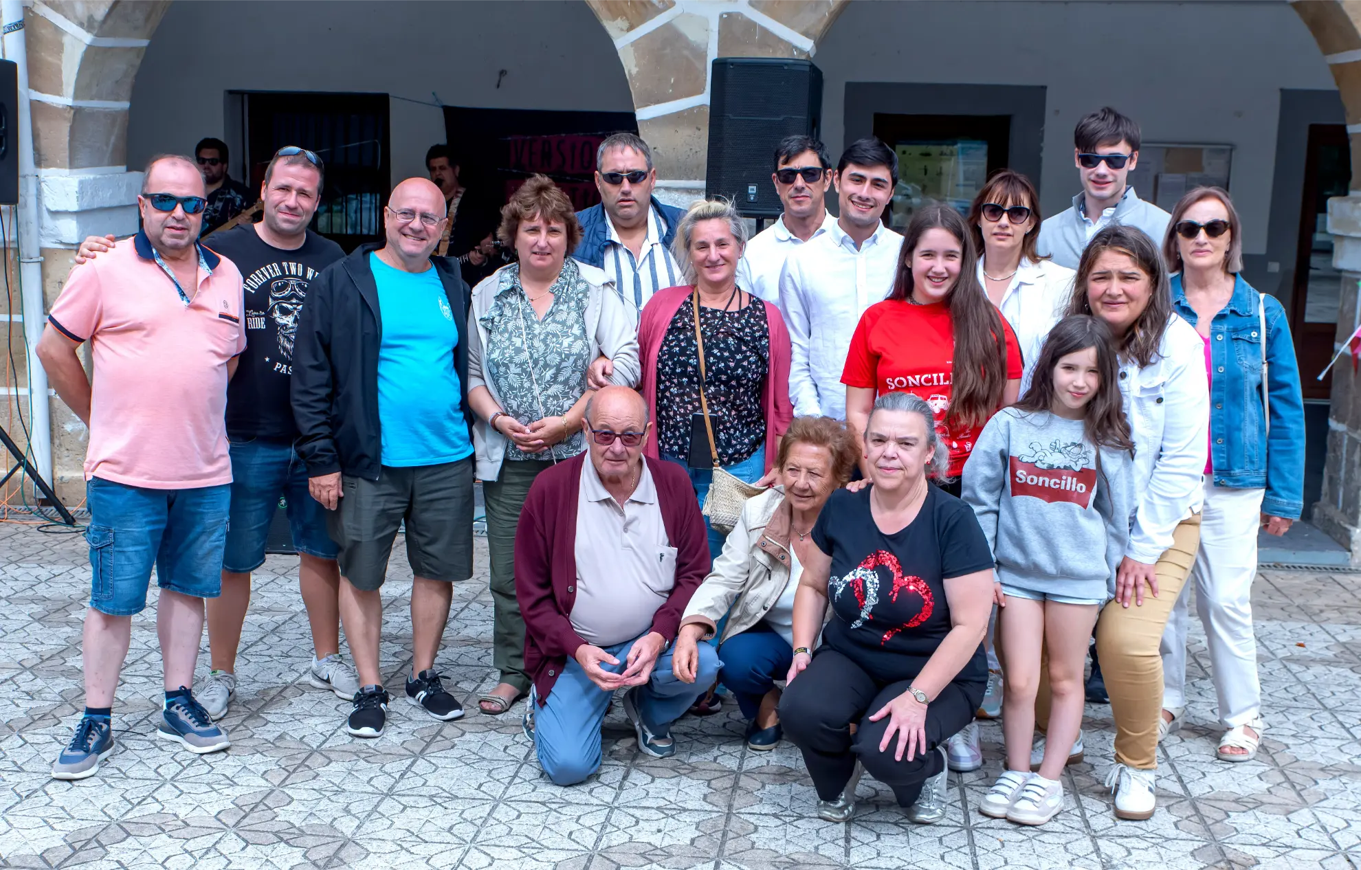 Un grupo de personas de varias edades posando juntas al aire libre delante de un edificio con arcos en la Quedada de Camiones Soncillo 2025, captando fotos memorables del evento.