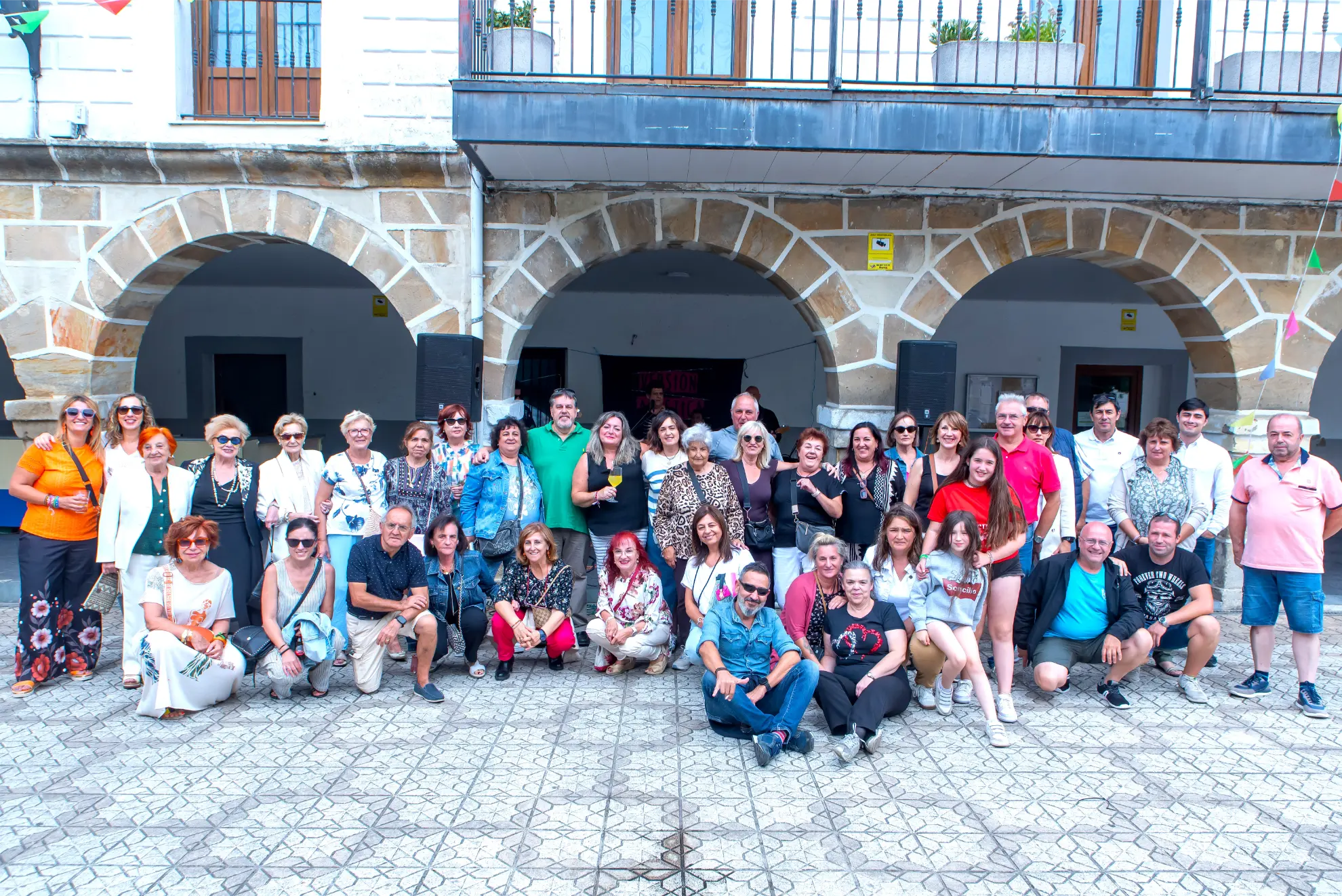 Un gran grupo de personas posando y sonriendo juntas delante de un edificio de piedra con arcos en el Soncillo 2025 Quedada de Camiones.