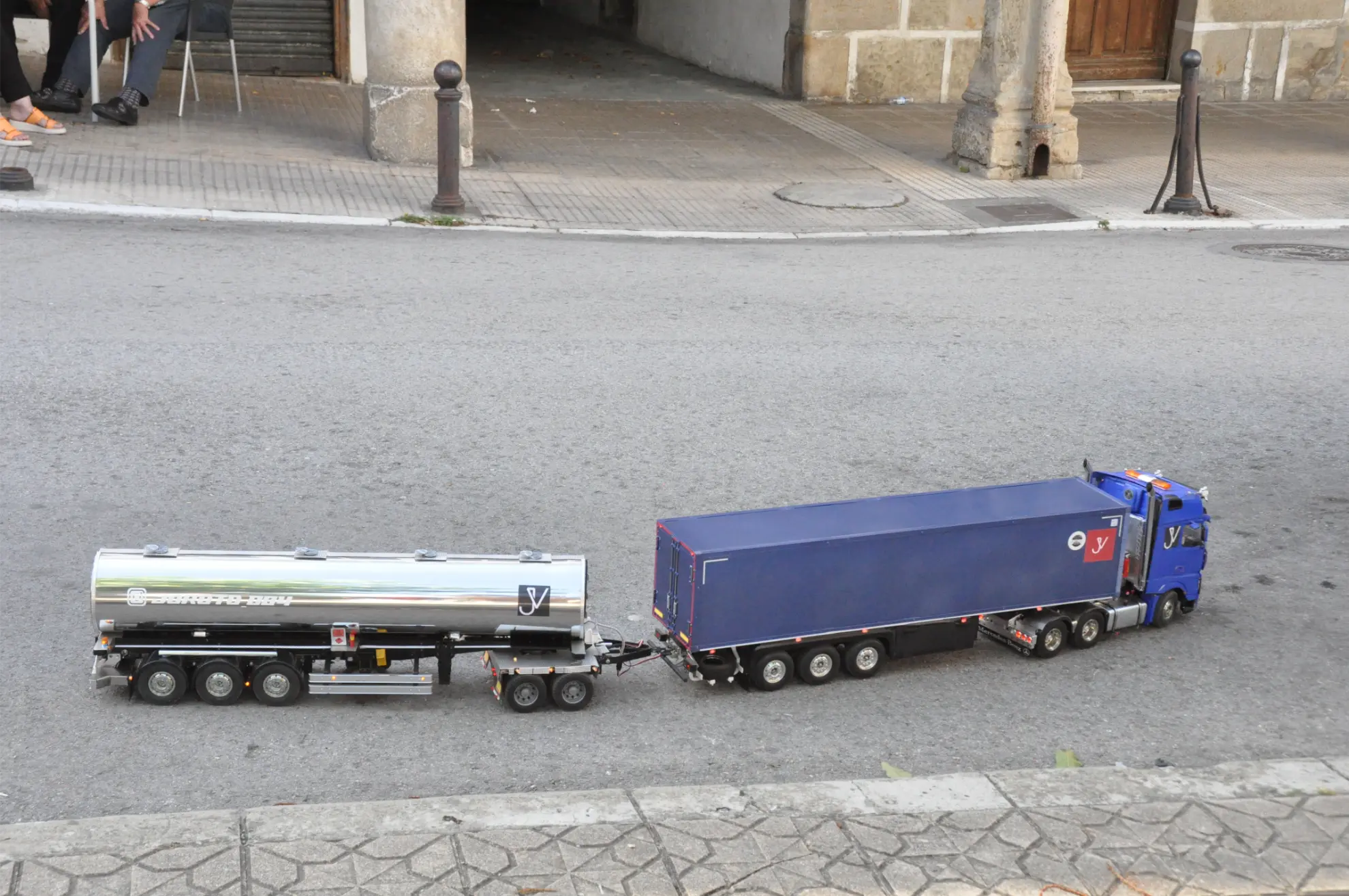 Dos detallados camiones de juguete, un camión cisterna y un camión contenedor azul, aparcados uno al lado del otro en una calle de la ciudad, perfectos para recrear tu propia Quedada de Camiones o escribir una crónica del Soncillo 2025 en miniatura.