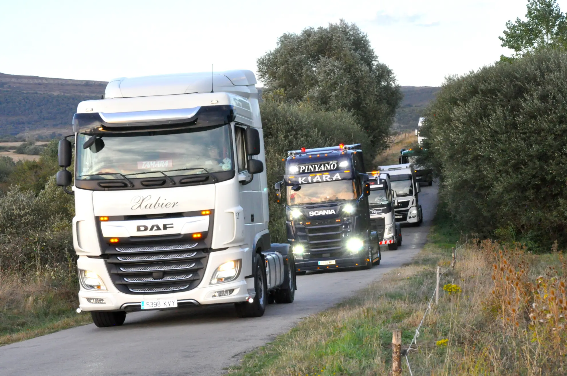 Cuatro grandes camiones circulan en fila por un camino rural rodeado de árboles y hierba durante la 2025 Quedada de Camiones en Soncillo.