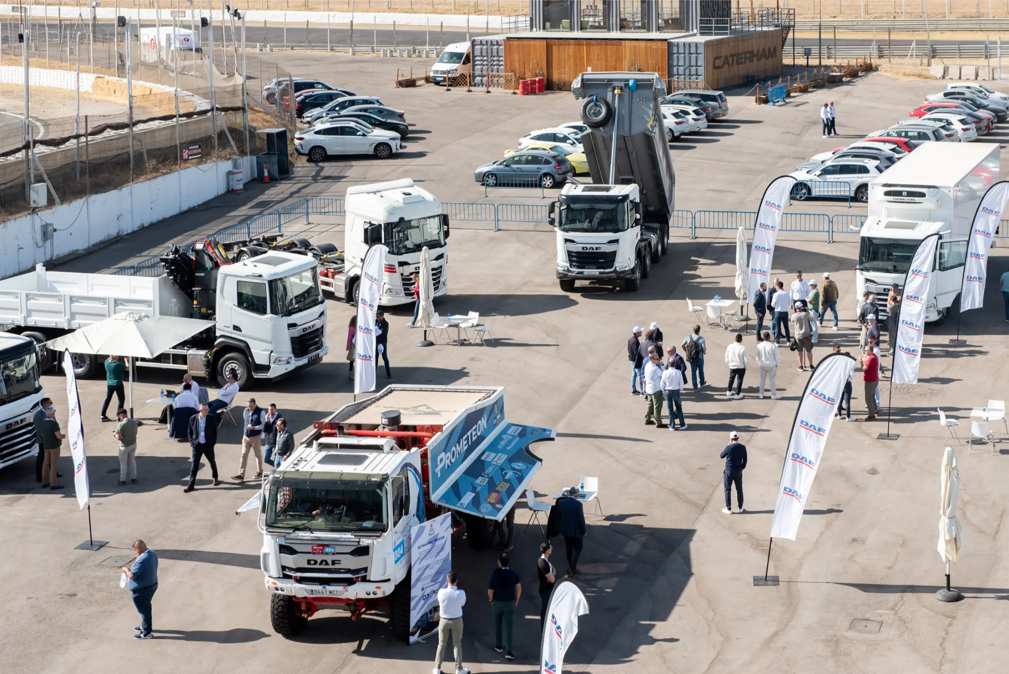 Vista aérea de una exposición de camiones con gente, camiones aparcados y pancartas informativas en un solar al aire libre.