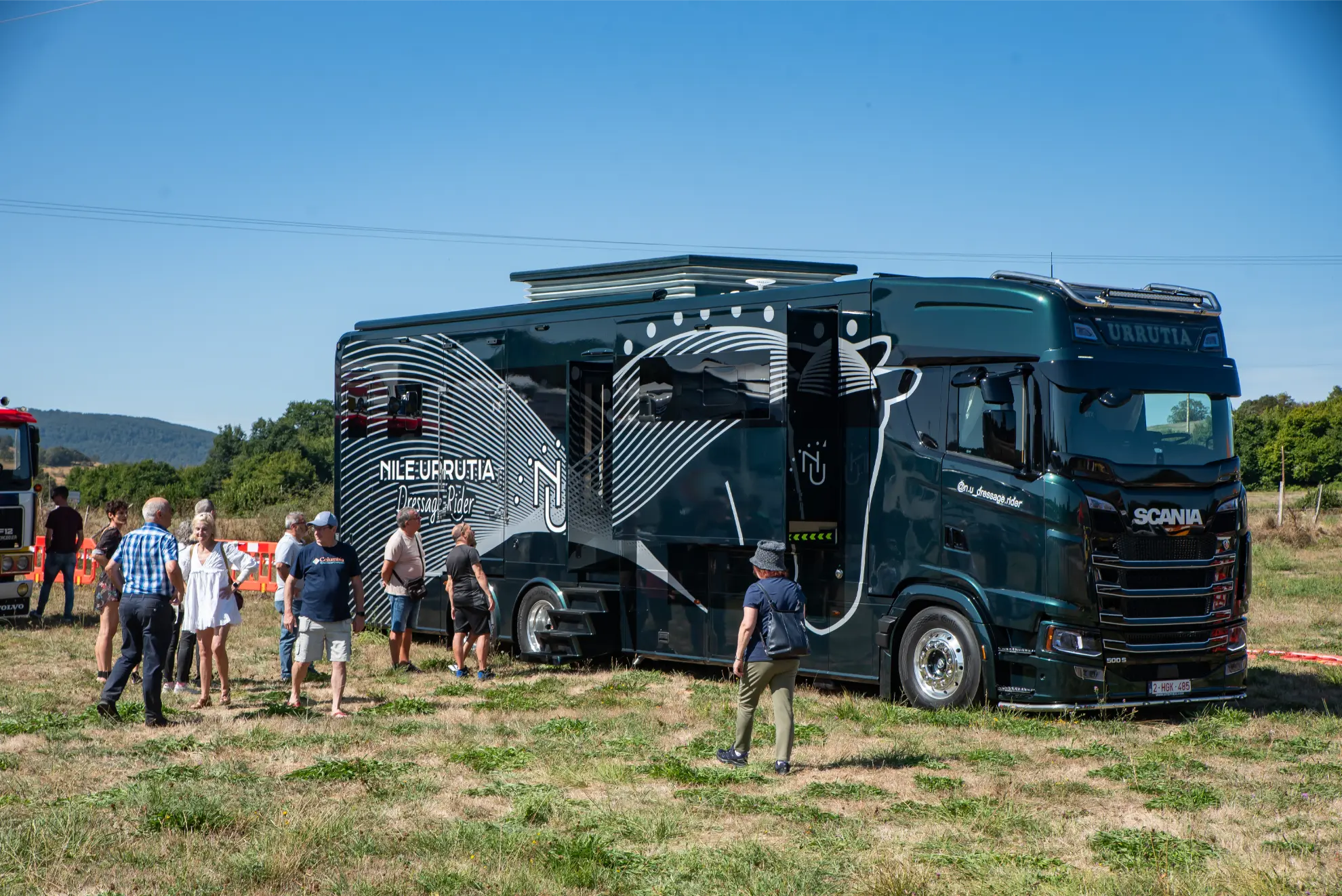 Un grupo de personas junto a una gran furgoneta Scania negra aparcada sobre hierba seca en la Quedada de Camiones Soncillo 2025, captando un momento de esta crónica única en una zona al aire libre.
