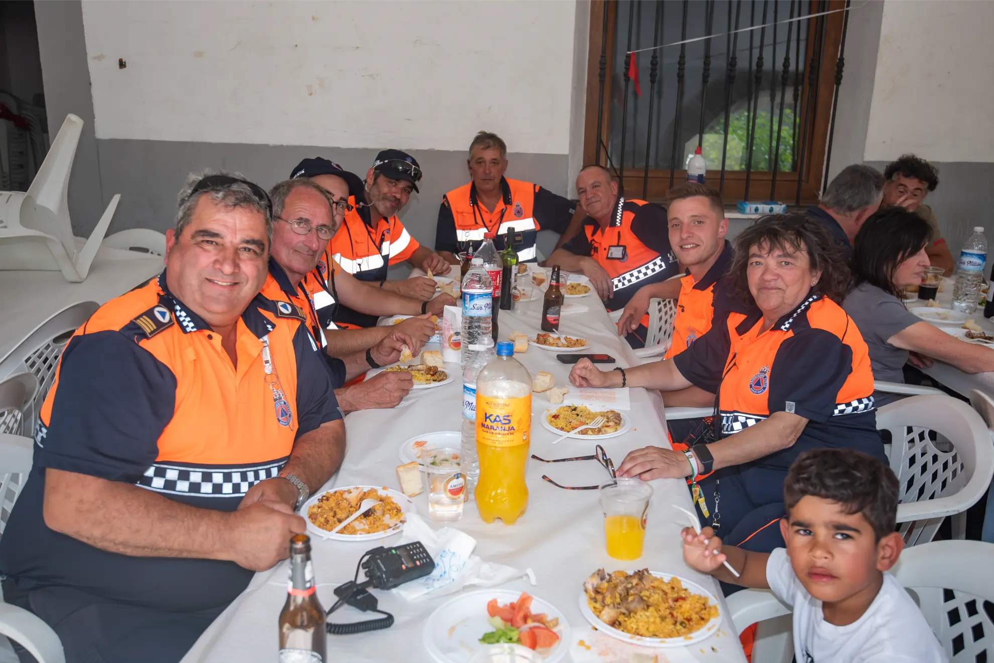 Un grupo de personas con uniformes naranjas comiendo juntos en una mesa, con un niño sentado delante -captado durante la Quedada Camiones 2025.