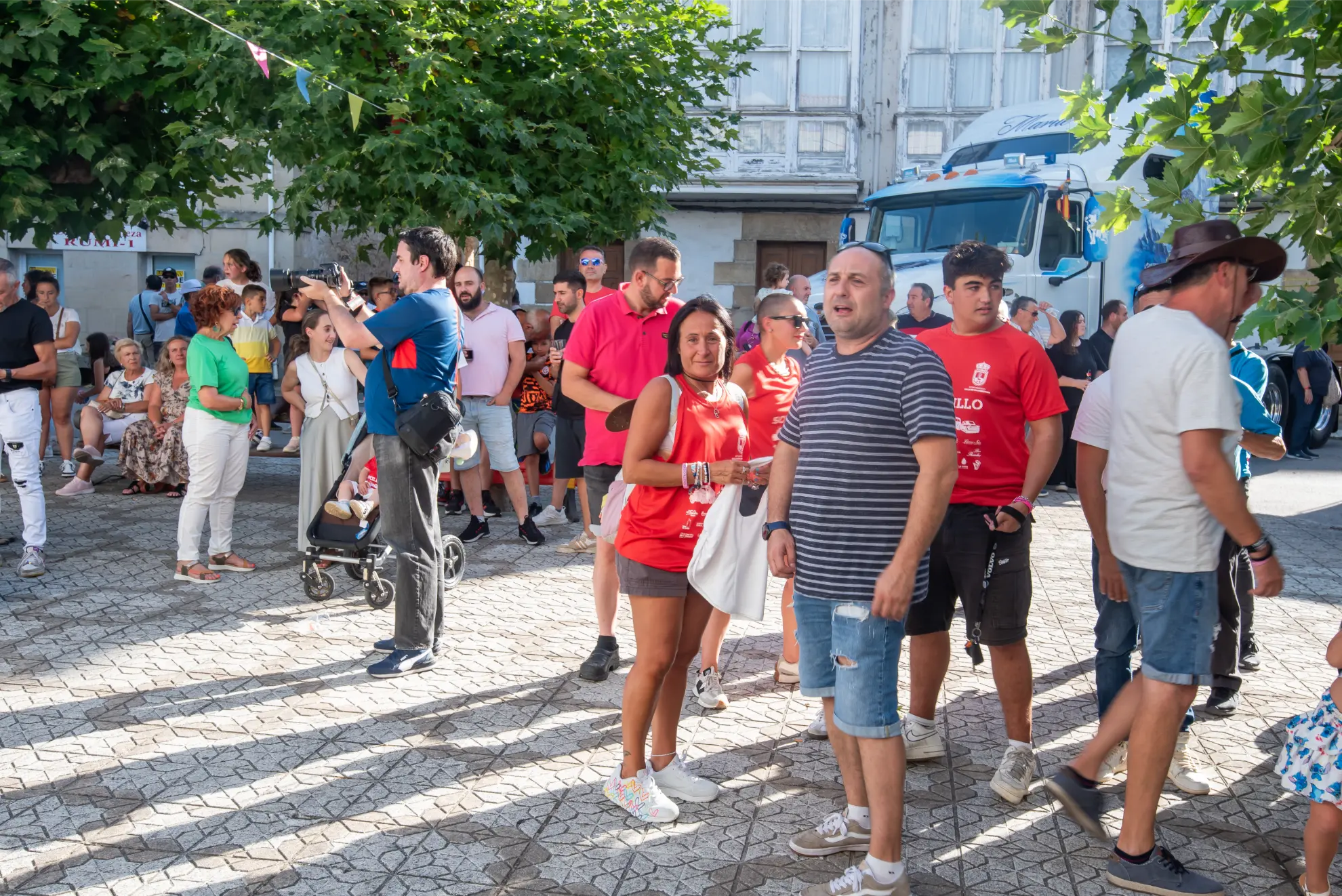 La gente se reúne al aire libre en un día soleado, algunos con camisetas rojas, con árboles y un camión de fondo durante la Quedada de Camiones Soncillo 2025.