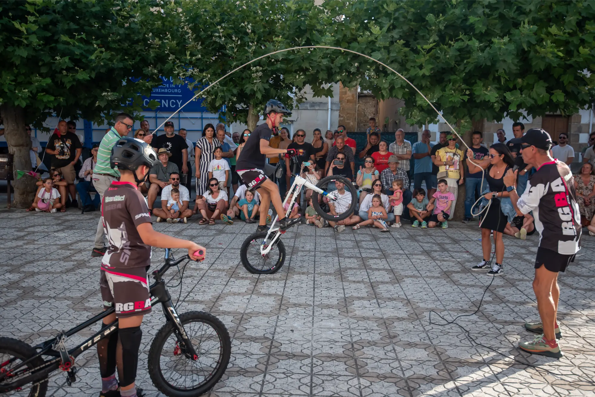 En la Quedada de Camiones Soncillo 2025, un ciclista salta a la comba sobre una bicicleta mientras una multitud observa al aire libre en un día soleado: ¡un espectáculo digno de crónica!.