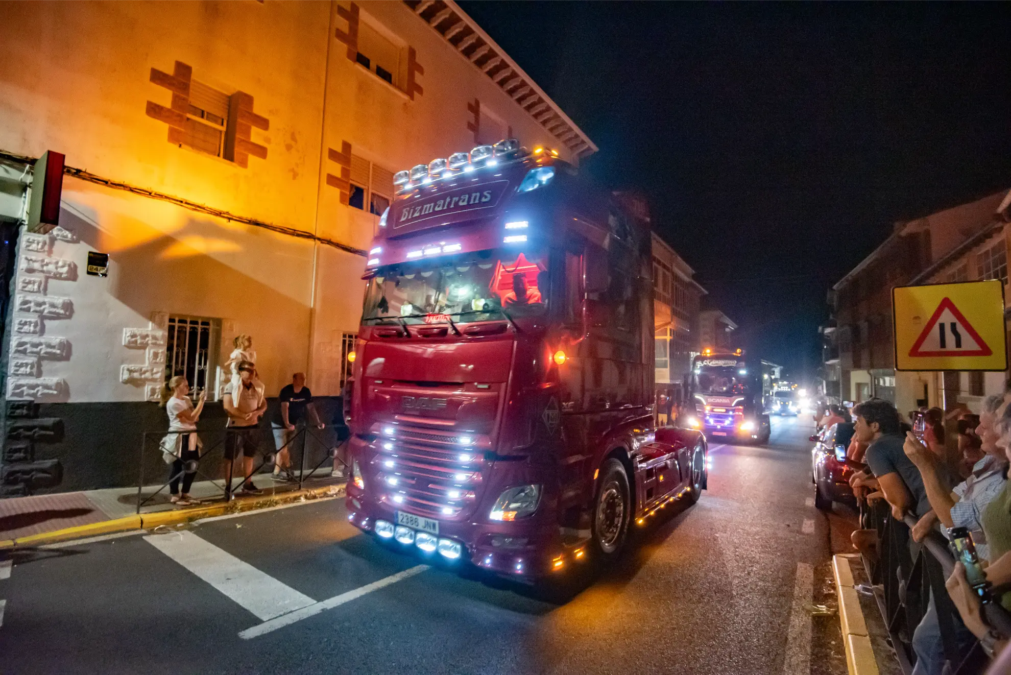 Un semirremolque rojo e iluminado atraviesa el desfile nocturno de la Quedada de Camiones en Soncillo 2025, con multitudes observando a ambos lados: una escena festiva digna de crónica.
