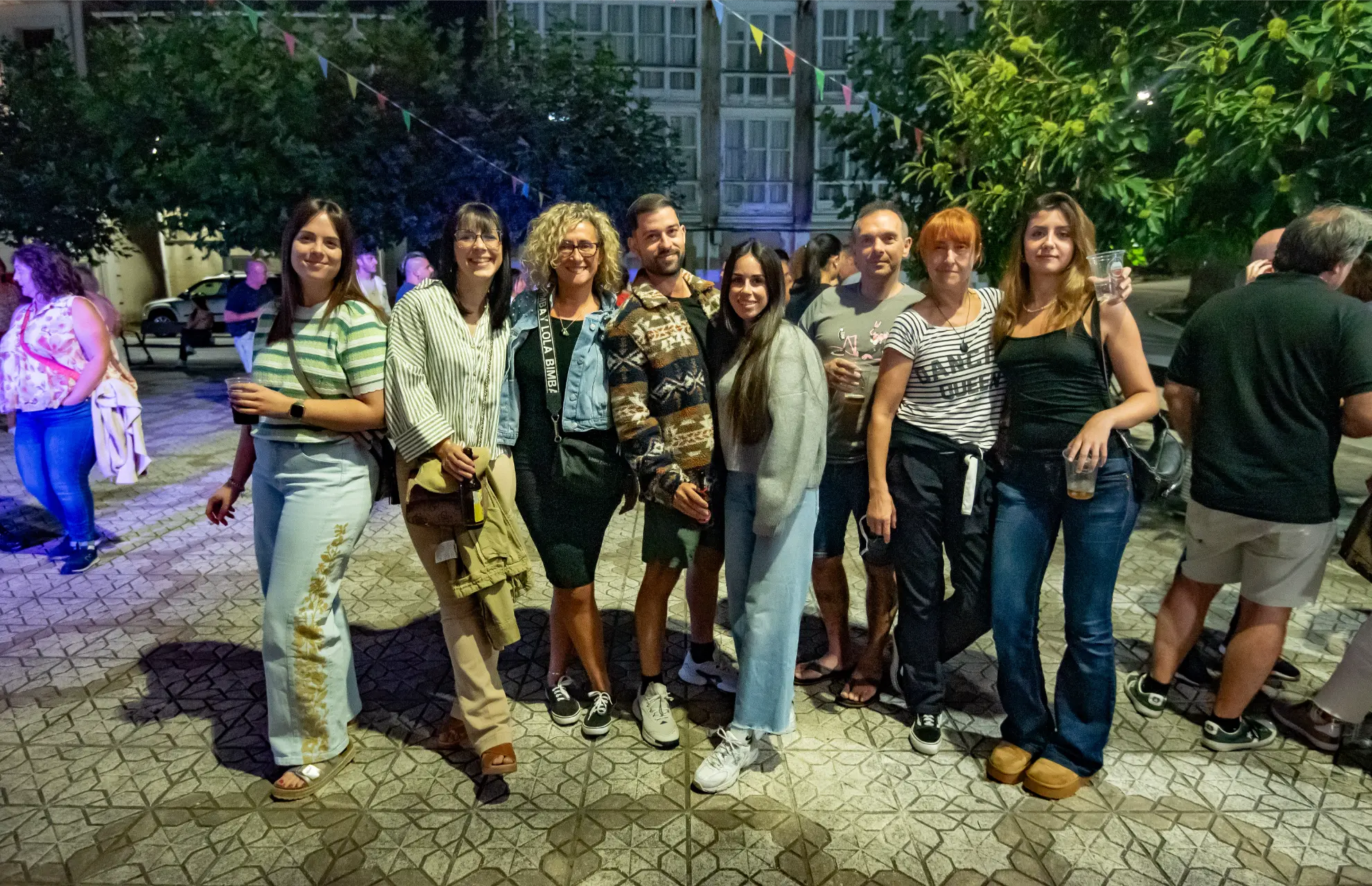 Un grupo de ocho personas sonriendo y posando juntas al aire libre en un evento nocturno, disfrutando del animado ambiente de la Quedada Soncillo 2025 entre camiones.