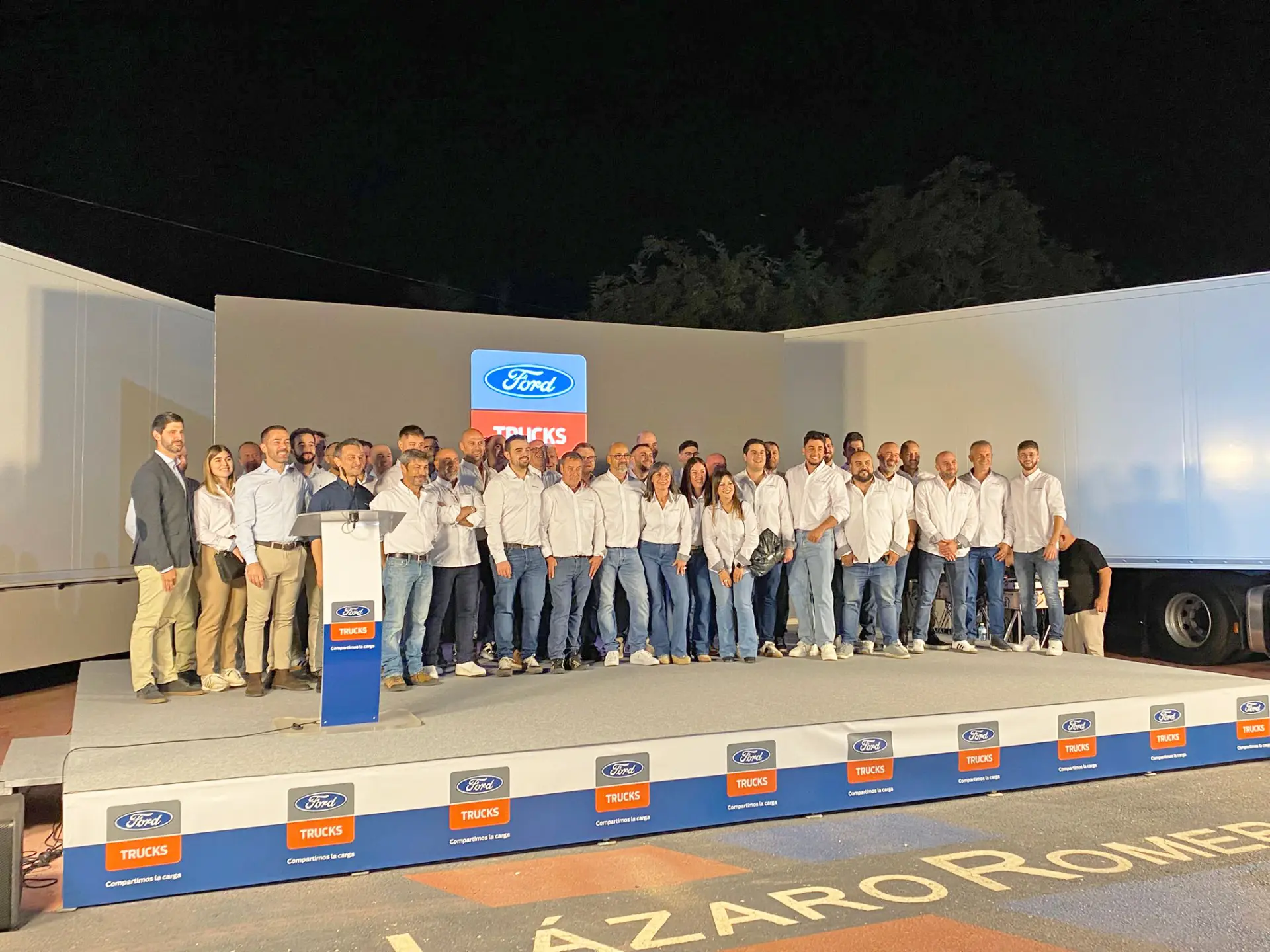 Un numeroso grupo posa en el escenario de un evento de Ford Trucks en Murcia, todos con camisas blancas y vaqueros, celebrando el lanzamiento del F-MAX GEN2.