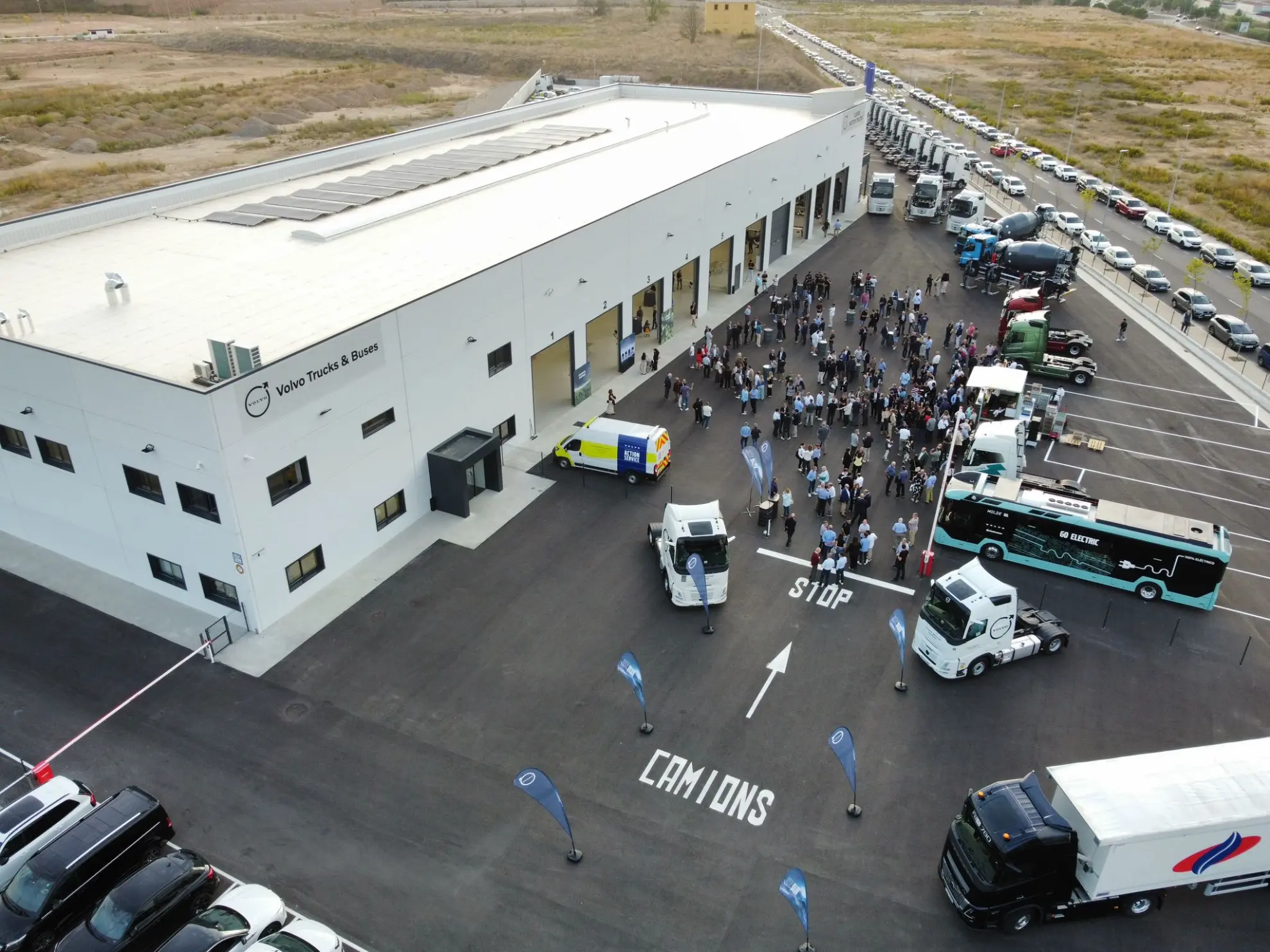 Una multitud se reúne frente a un gran edificio, con camiones, furgonetas y coches -algunos marcados con el distintivo Borrador automático- aparcados en los alrededores.