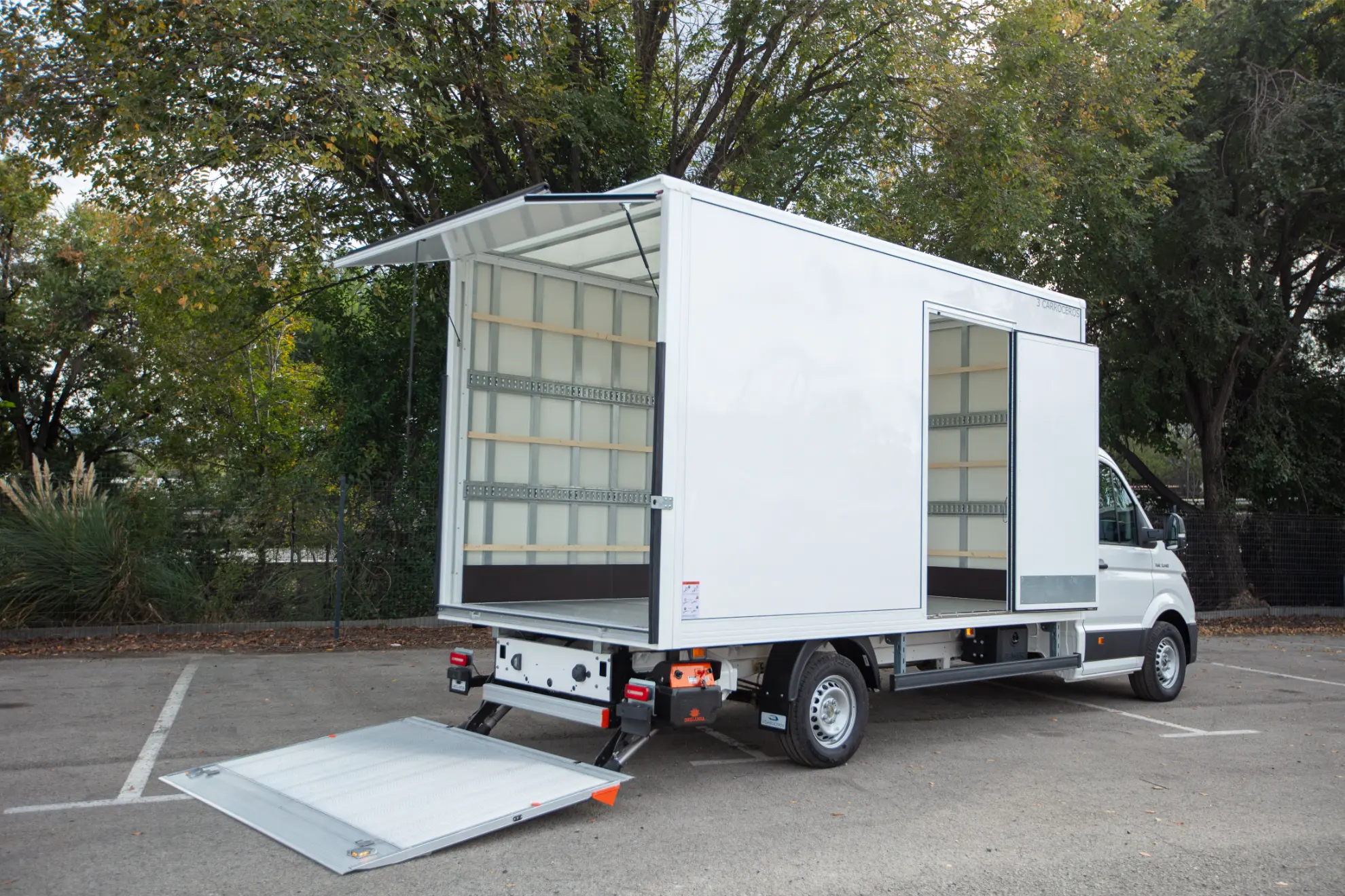Un camión MAN TGE blanco con puertas laterales y traseras abiertas, mostrando estanterías vacías y una rampa trasera rebajada-ideal entre las mejores furgonetas para reparto y furgonetas carrozadas.