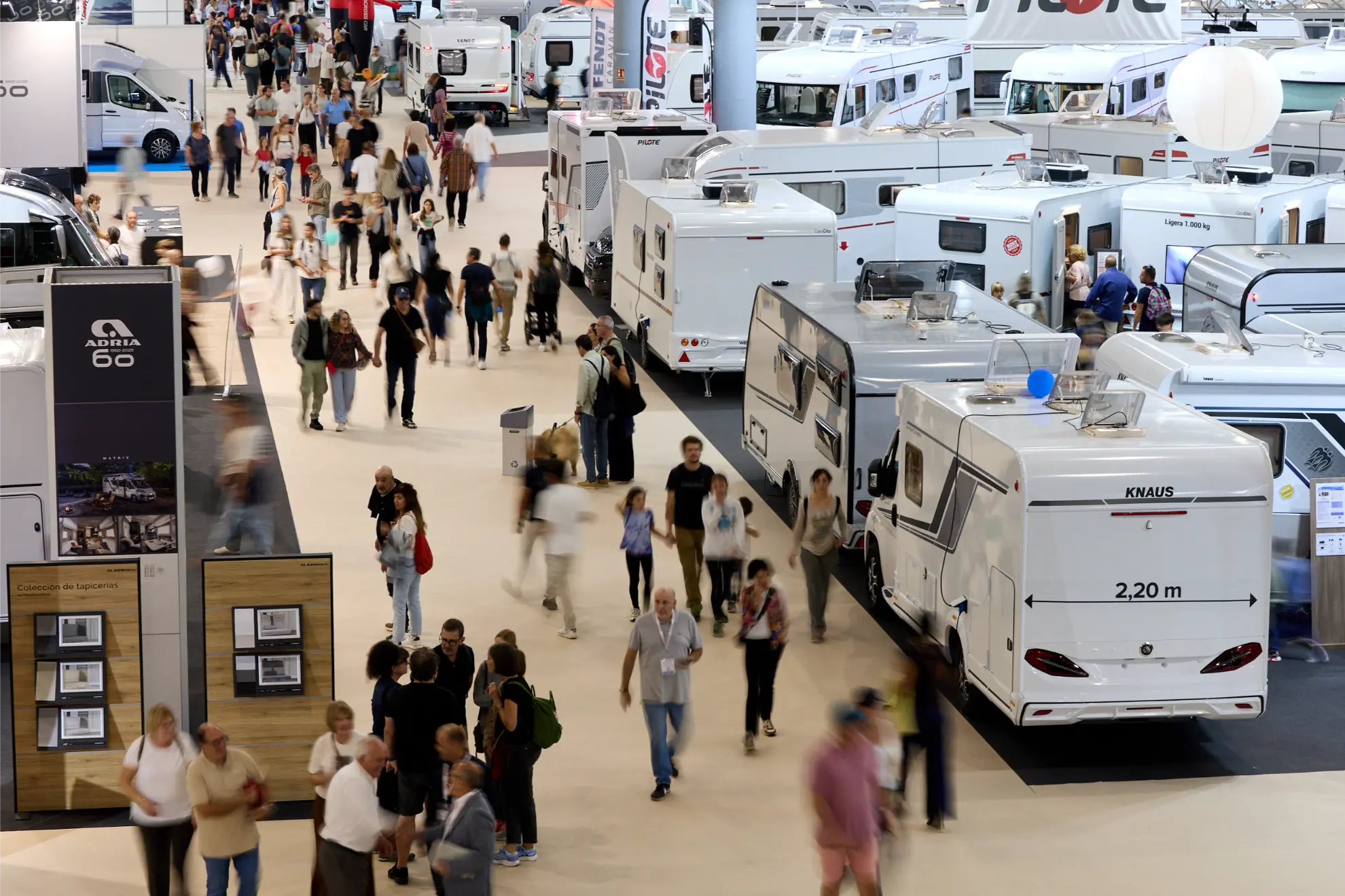Multitudes pasean entre hileras de autocaravanas y autocaravanas en el Salón del Caravaning, explorando los últimos modelos en esta exposición cubierta.