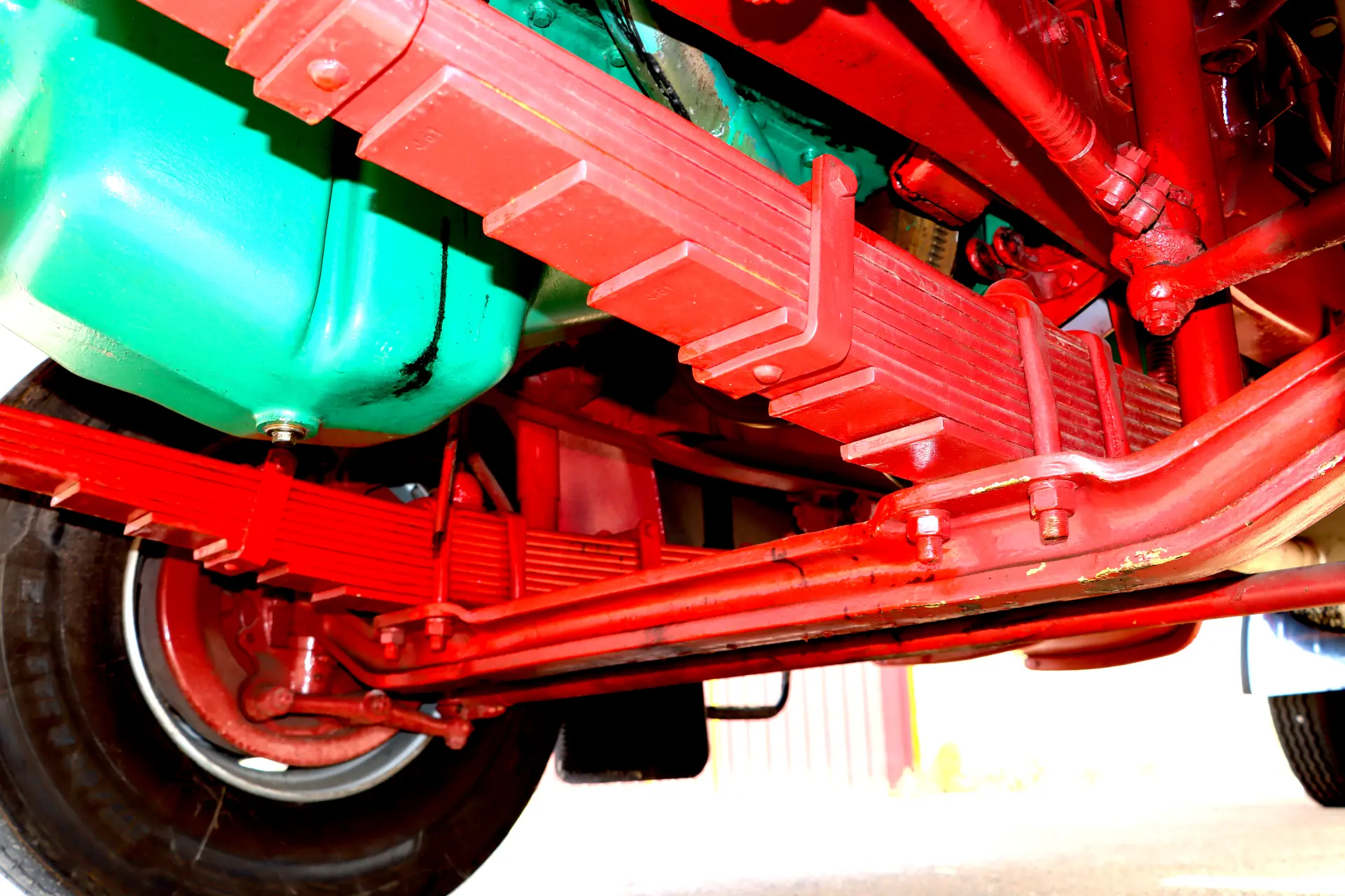 Primer plano del sistema de suspensión de un vehículo rojo y de los componentes verdes del motor, tomados desde abajo.
