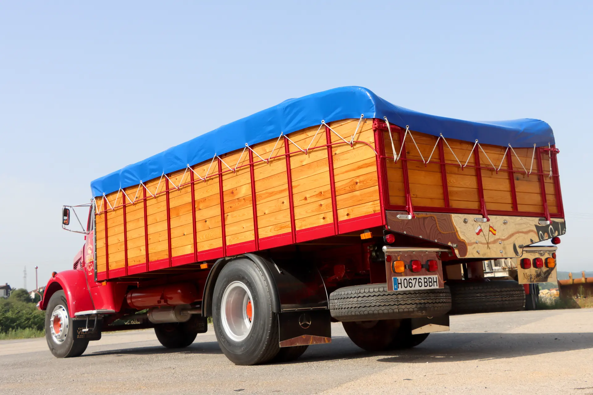 Camión rojo de época con caja de carga de madera y lona azul aparcado en un día soleado, perfecto para los aficionados a los camiones clásicos restaurados y a los vehículos históricos camiones.
