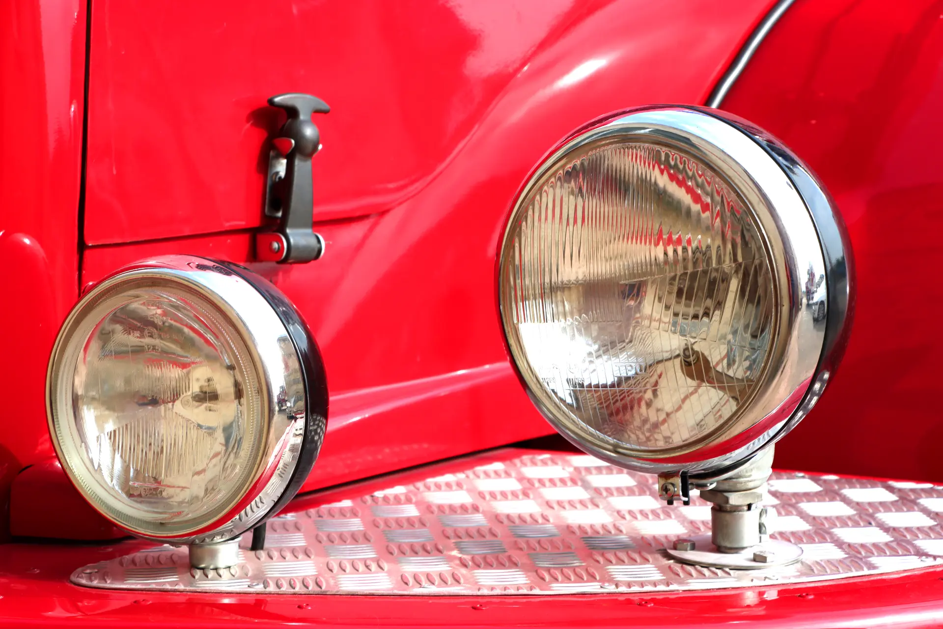 Primer plano de dos faros redondos en un coche rojo brillante de época con una superficie metálica a cuadros debajo de ellos.